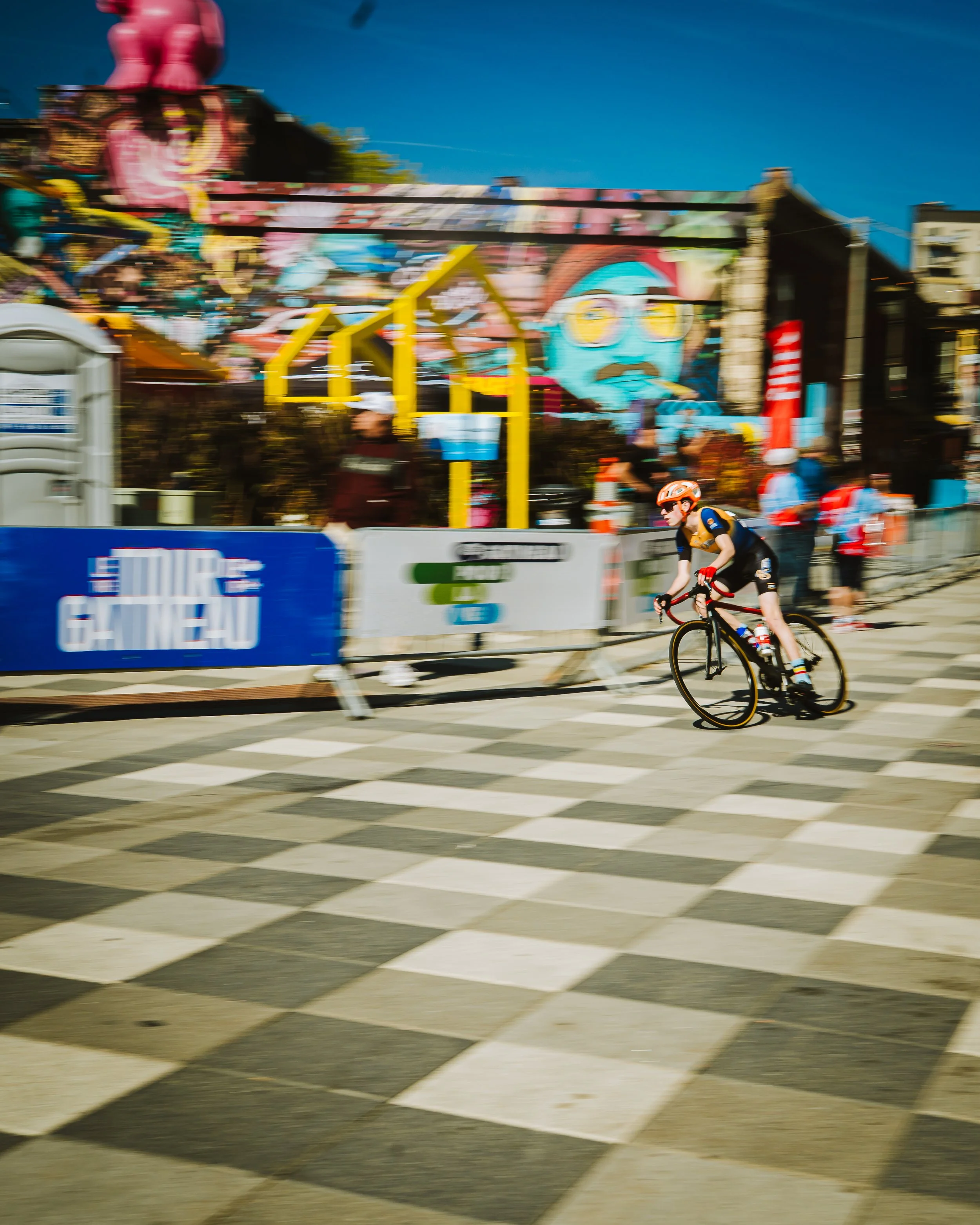 A cyclist wearing a helmet rides on a checkered crosswalk near a colorful amusement park with graffiti murals, during a sunny day.