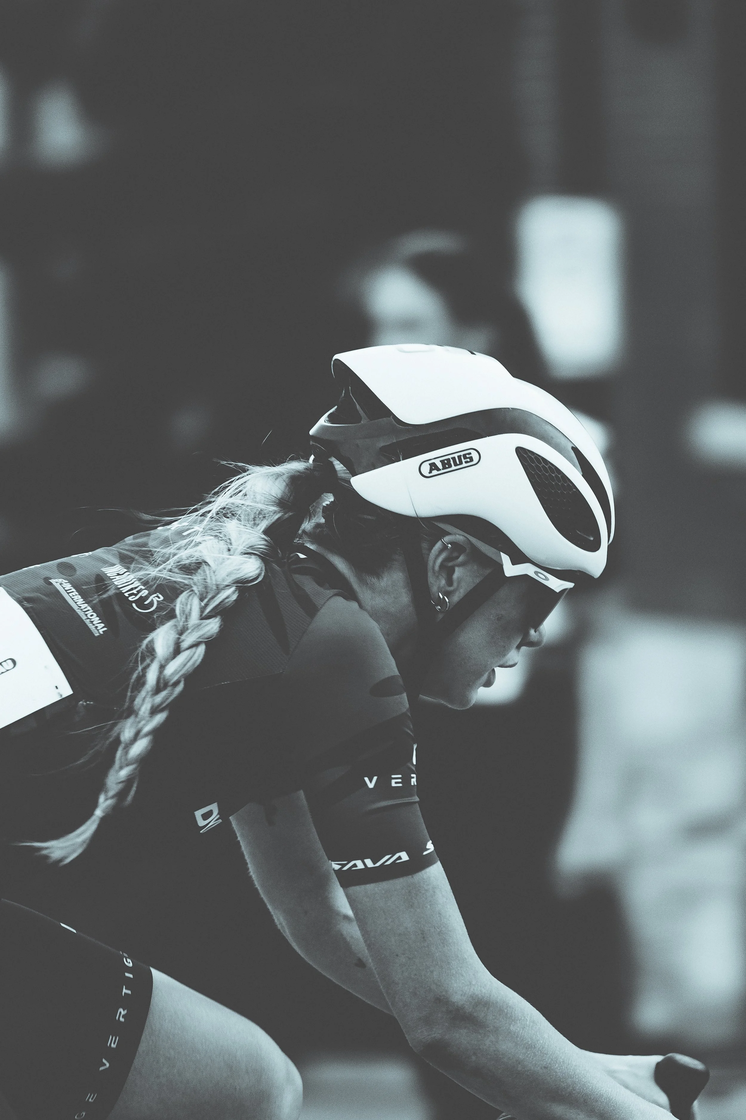 A female cyclist wearing a helmet, sunglasses, and a cycling uniform, leaning forward on her bike during a race.
