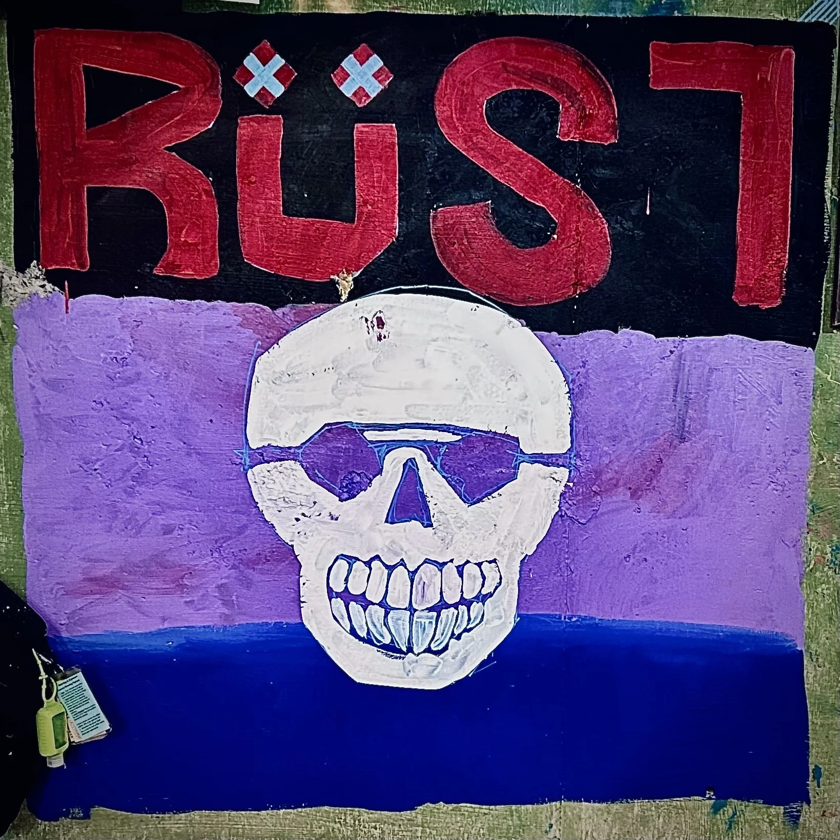 A colorful chalk drawing featuring a large white skull with purple shading, below the word 'RÜST' in bold red letters, with a background of contrasting colors.