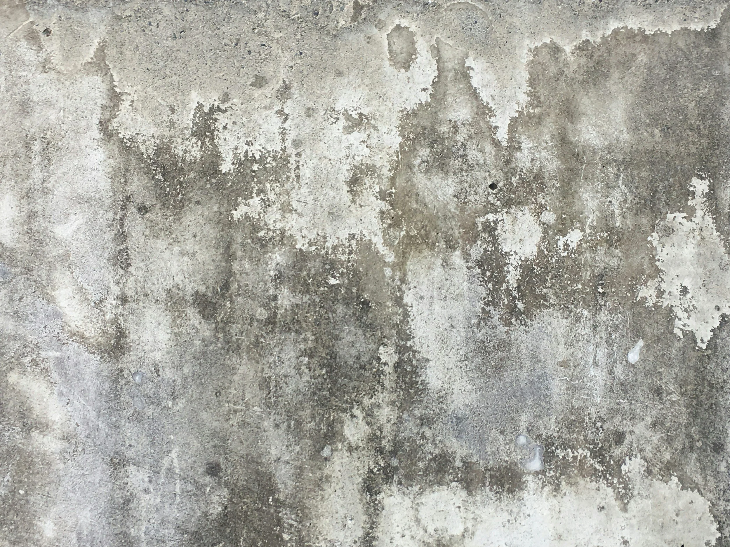 Close-up of a concrete or cement surface with weathered and worn texture, showing discoloration and patches of dirt or stains.