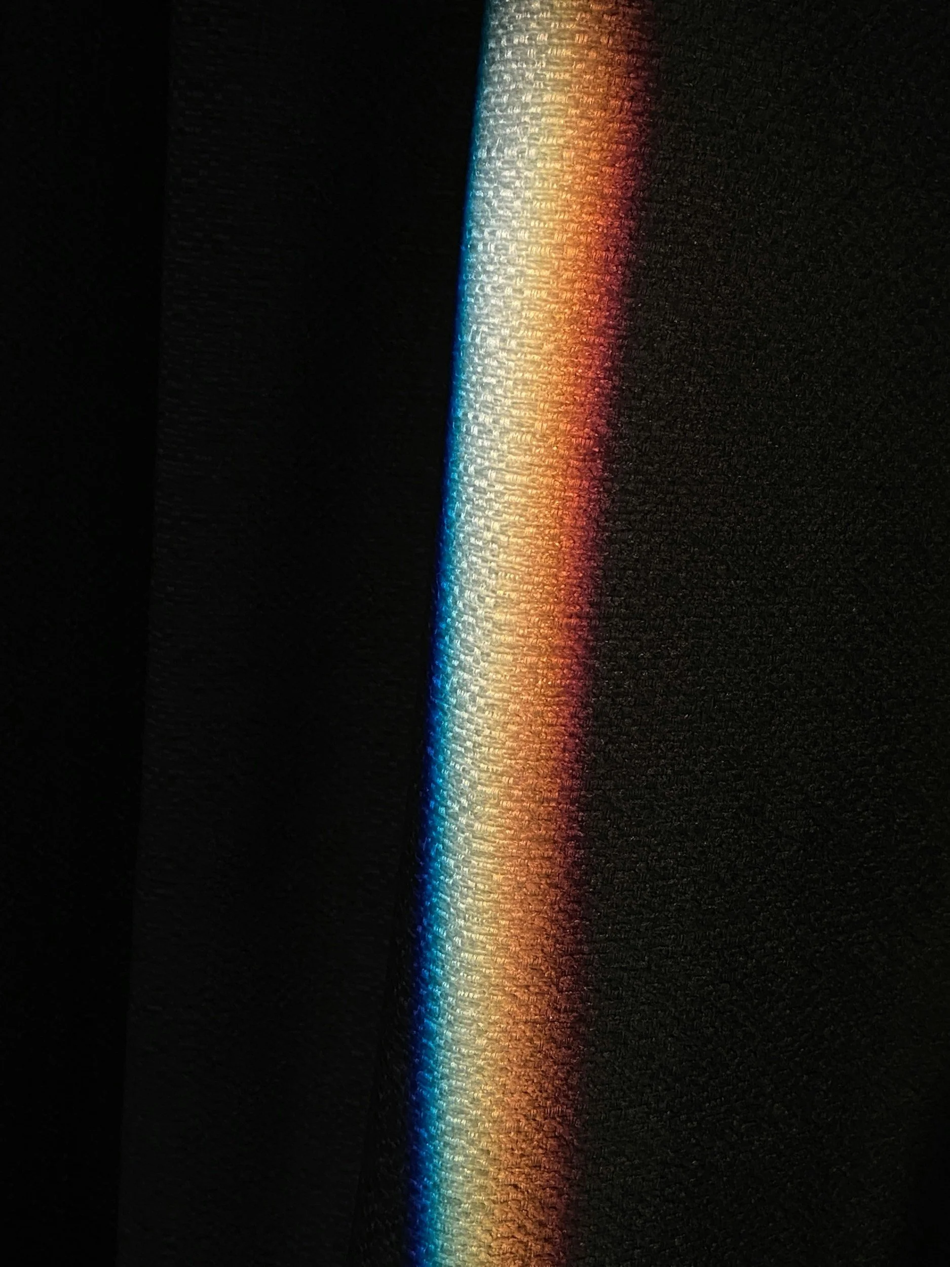 A beam of sunlight passing through a prism, creating a rainbow spectrum of colors on a dark textured surface.