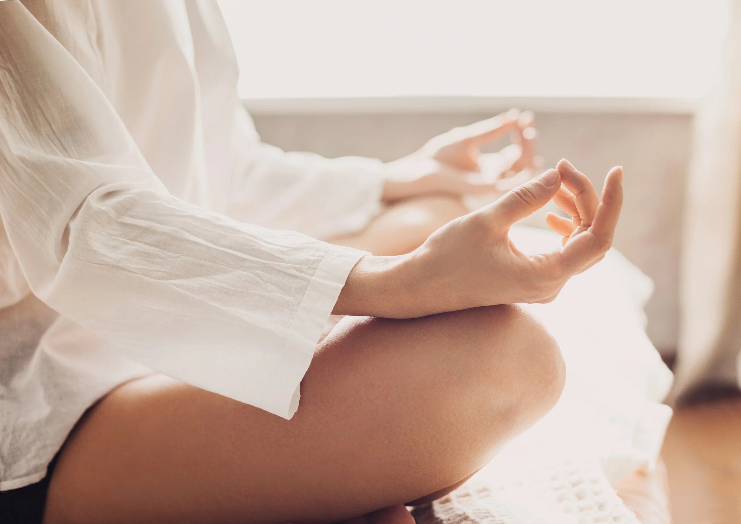 Meditative seated posture with hands in a mudra and rested on knees. White robes. Sunny room. Zen