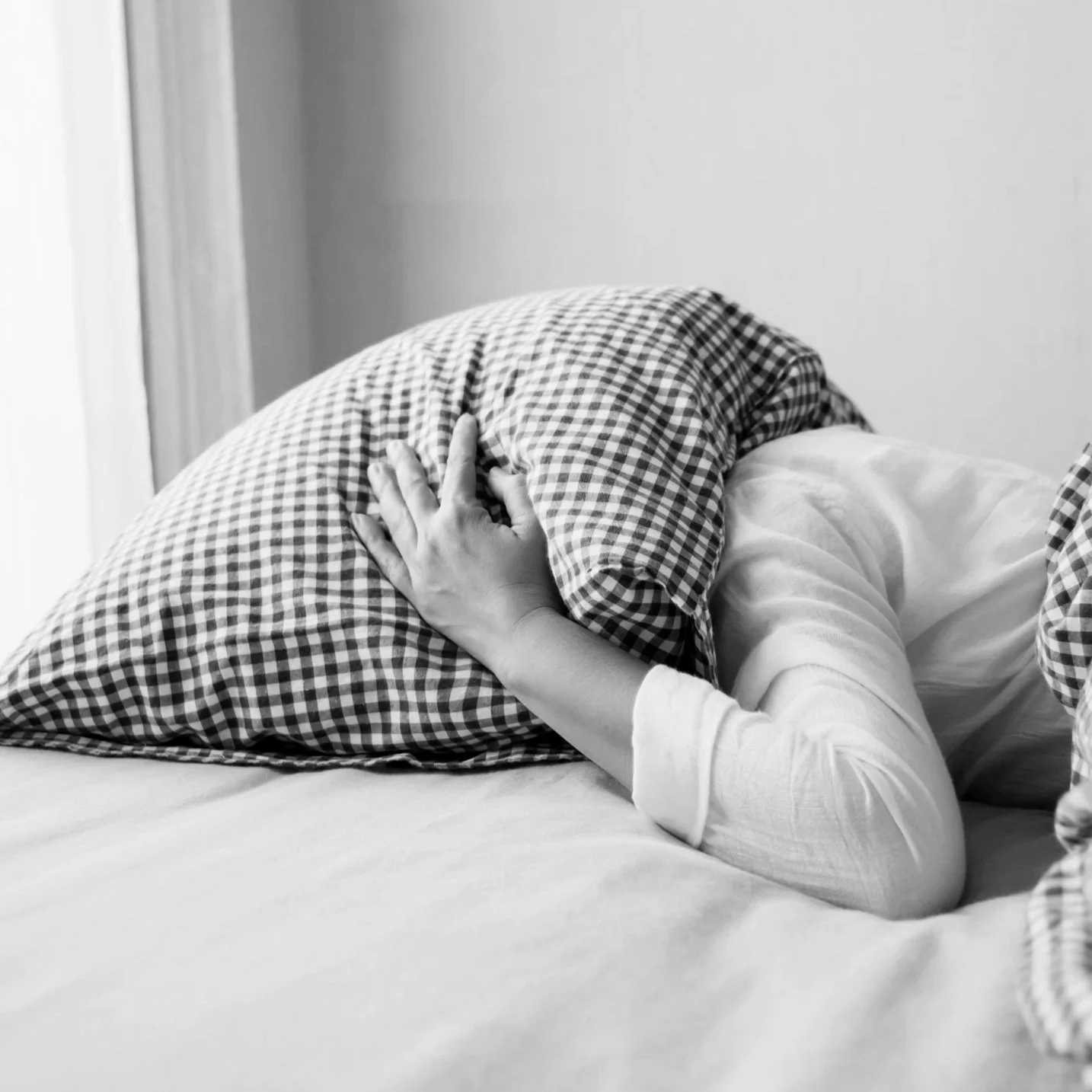 A person lays face down in bed with a pillow held in place over their head with a hand because the headache pain is so bad they need Retreatment Wellnessd