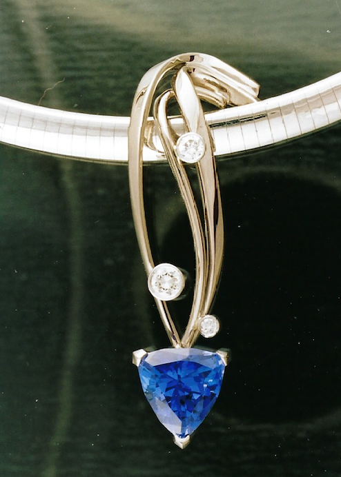 A silver necklace with a blue heart-shaped gemstone and three small clear diamonds hanging from a white cord.