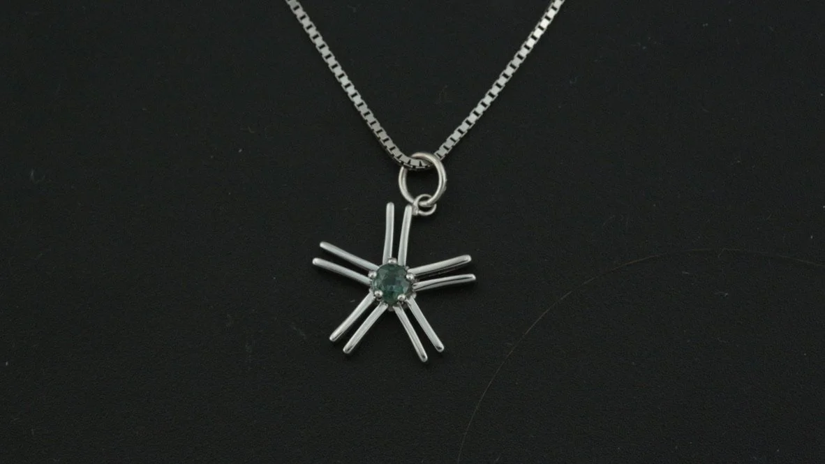 Silver star-shaped pendant necklace with a central green gemstone on a black background.