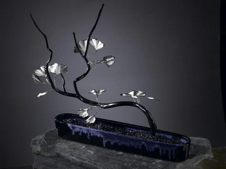 Stark Jewelers' handmade sculpture featuring sterling and bronze gingko leaves on a bonsai shaped branch in a handmade indigo blue and black drips vase