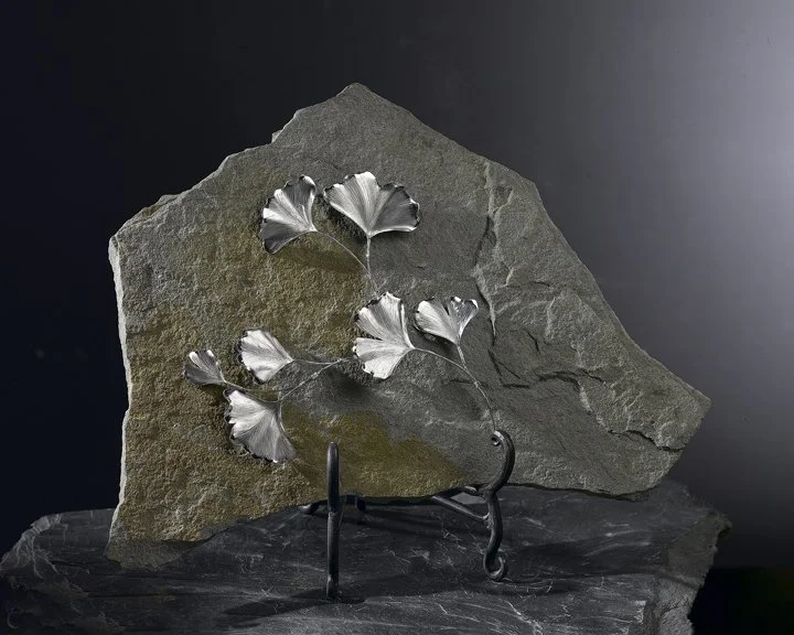 A Stark Jewelers hand engraved gingko leaves on a gray stone plate with yellow earth hue wall art