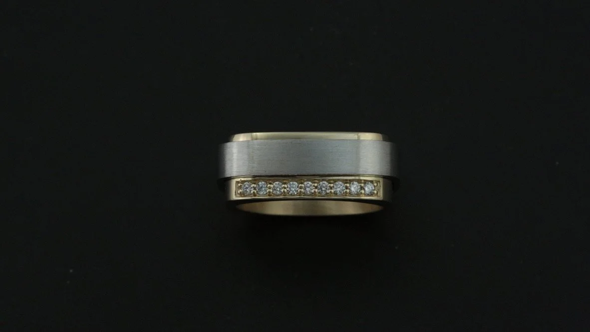 A silver and gold men's wedding band with embedded diamonds against a black background.