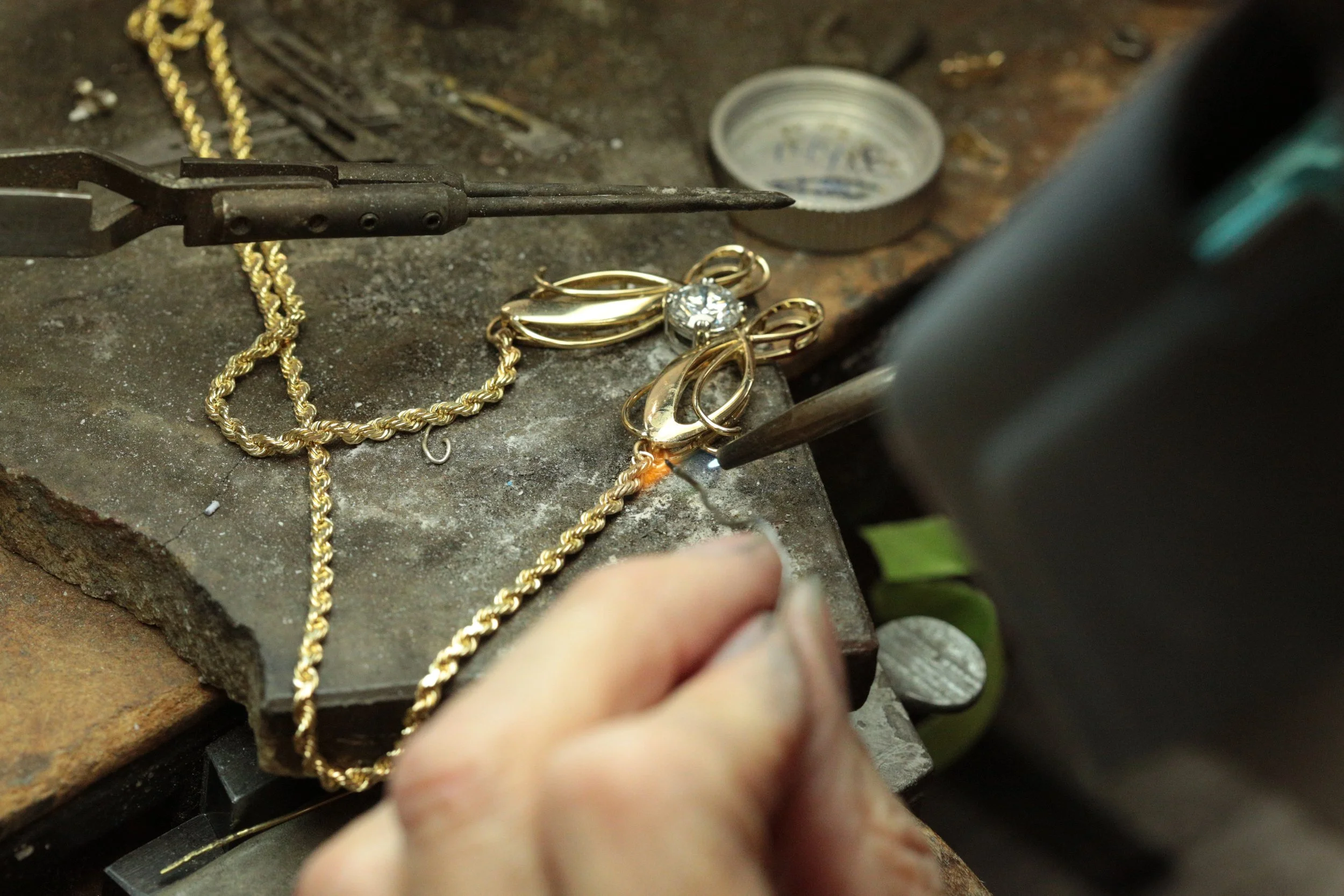 the jeweler carefully applying the torch to permanently solder the chain directly to the pendant's framework, creating a seamless and secure necklace.