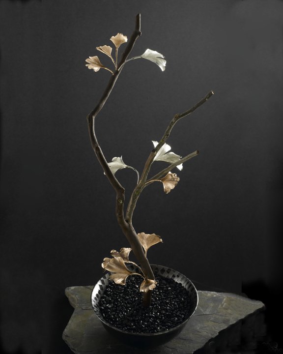 A stark Jewelers Sculpture with natural tree branch with hand carved bronze and sterling silver gingko leaves placed on the branch like a beautiful bonsai plant in life