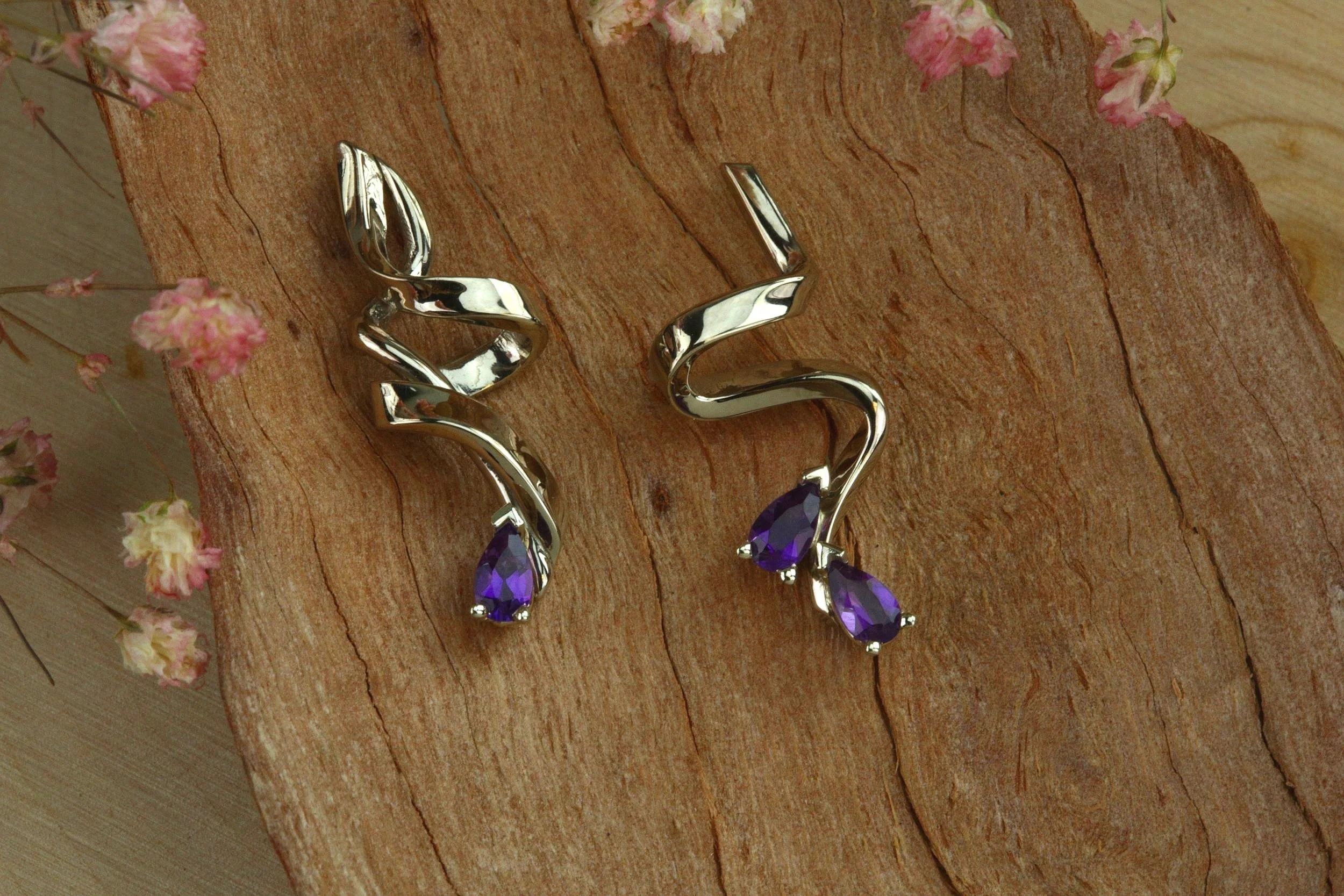 Pair of curl and ribbons style gold earrings featuring pear shape amethyst designed and handmade by stark jewelers