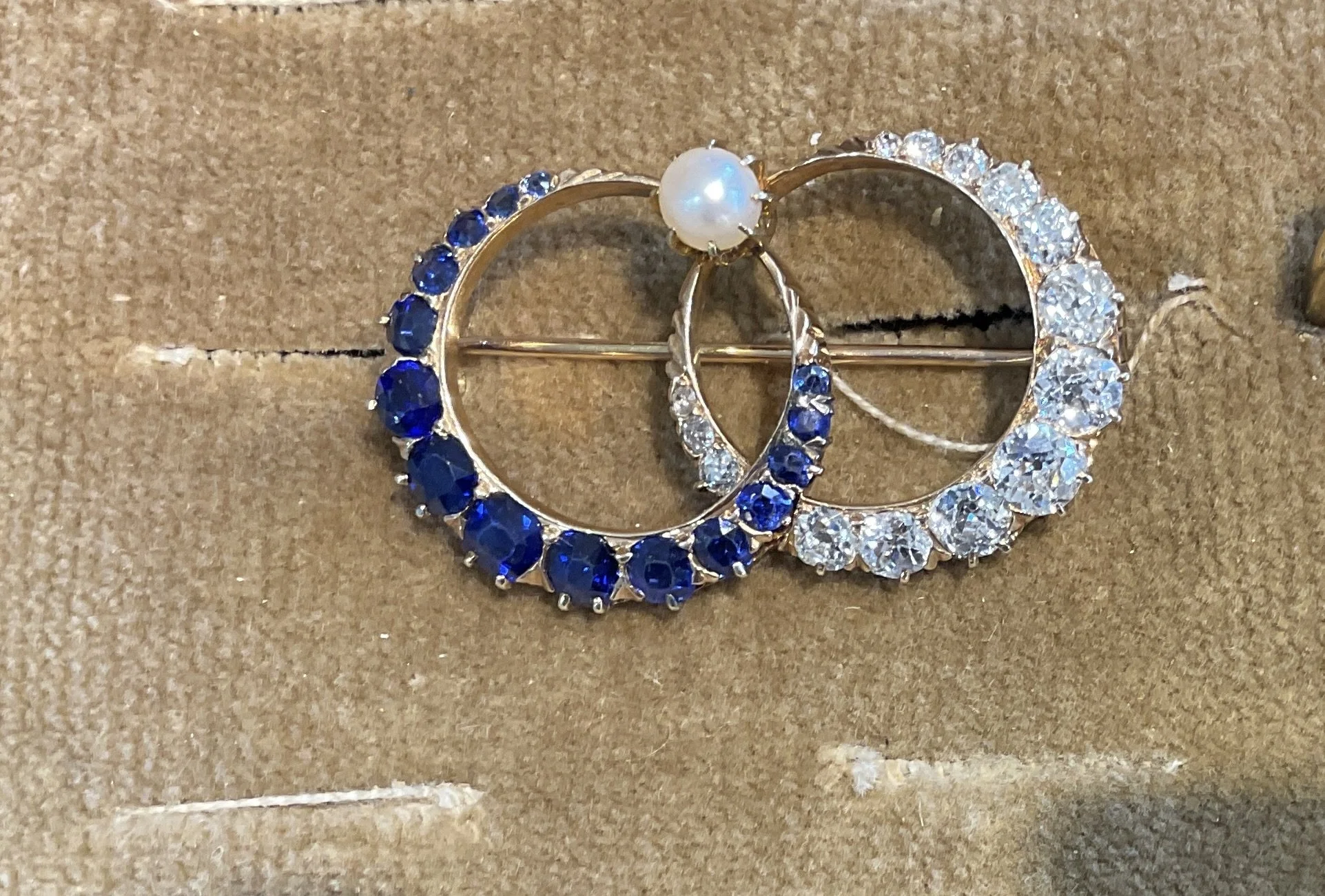 a vibrant, deep blue sapphire surrounded by a brilliant halo of diamonds, all set in a classic yellow gold brooch frame before heirloom transformation at Stark Jewelers in Sacramento