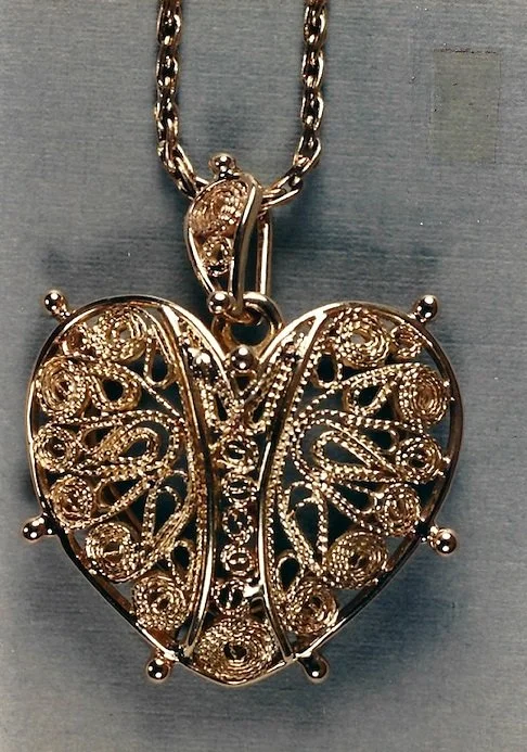 Gold heart-shaped locket with intricate filigree design, hanging from a gold chain.