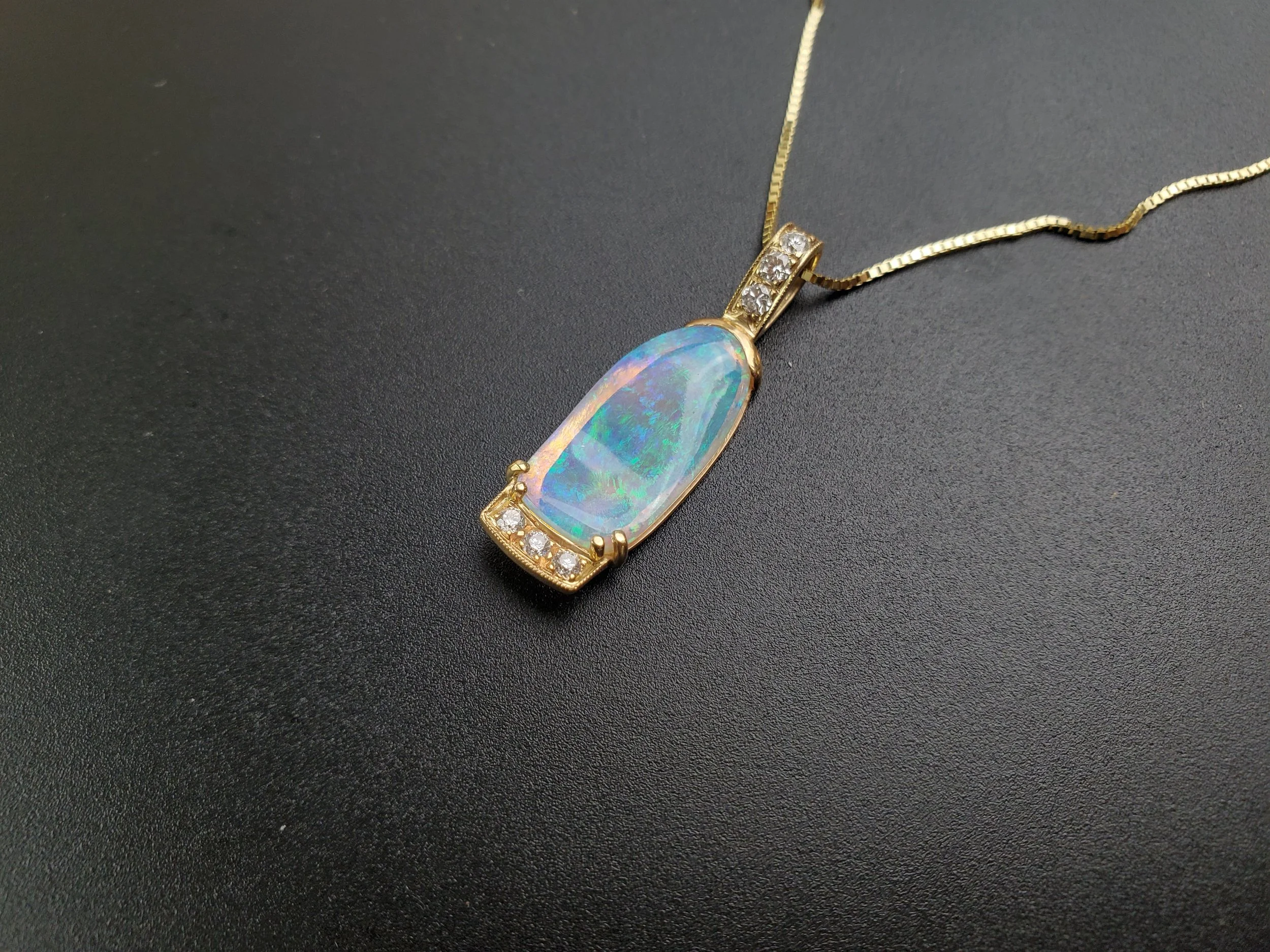 A gold necklace with an opal pendant and small diamonds on a black surface.
