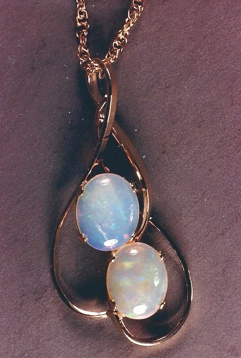 Gold necklace with a pendant featuring two oval opal stones surrounded by an abstract gold frame.