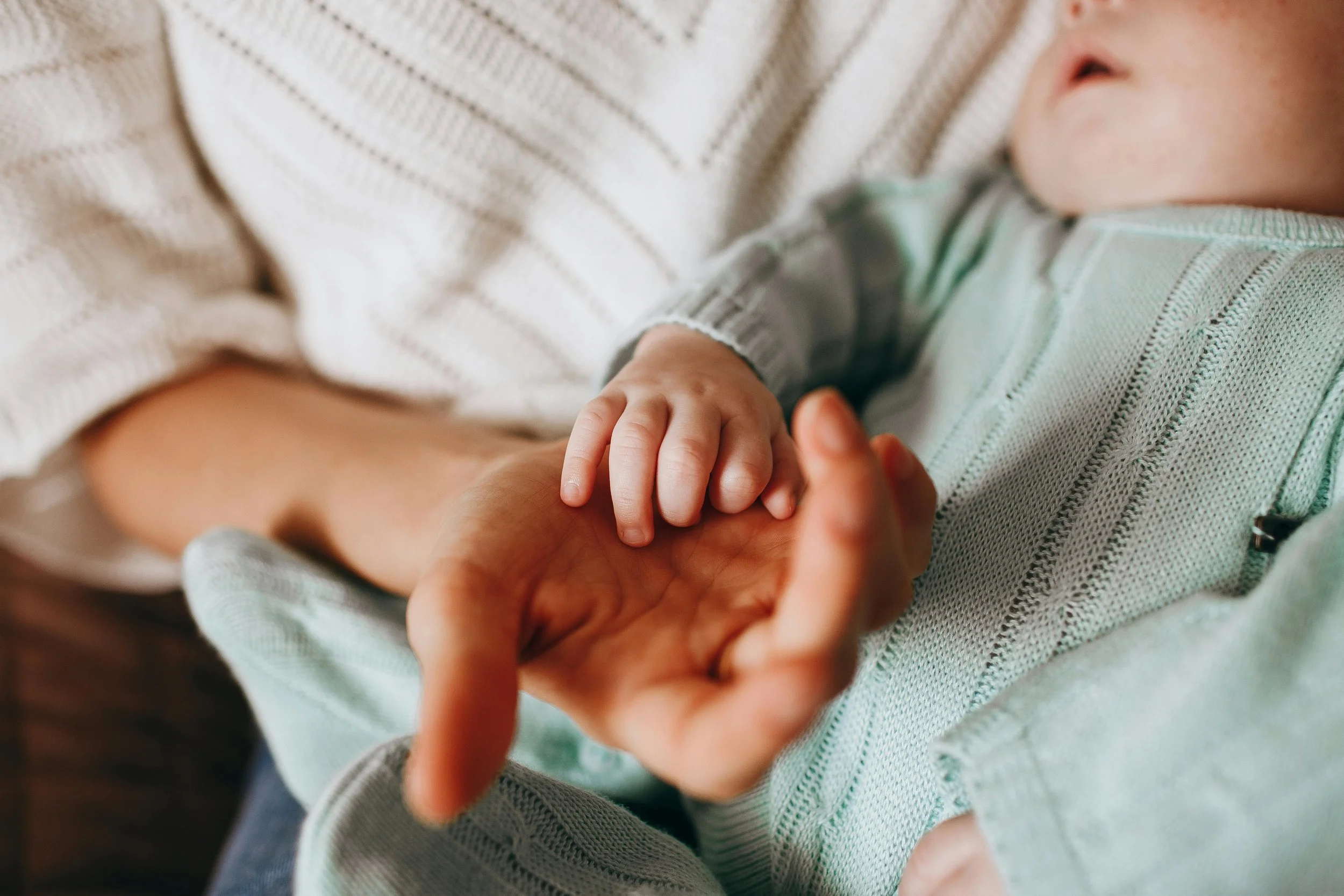 Soft-focus close-up of hands holding a child’s hand, emphasizing the "Gold Forged for a Lifetime" by Stark Jewelers