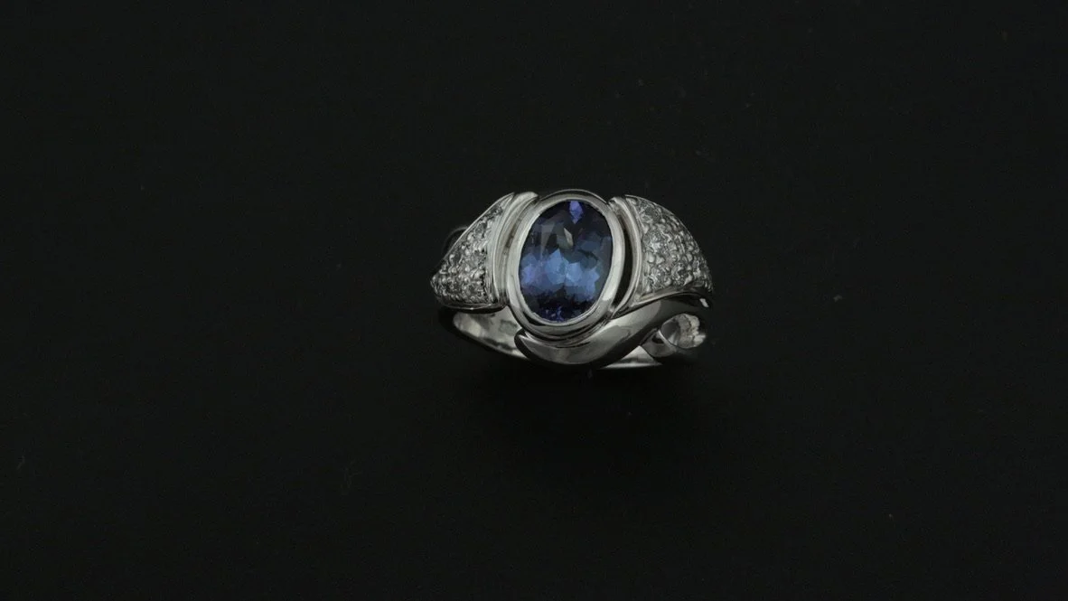 Silver ring with a large oval dark blue gemstone and small surrounding clear stones on a black background.