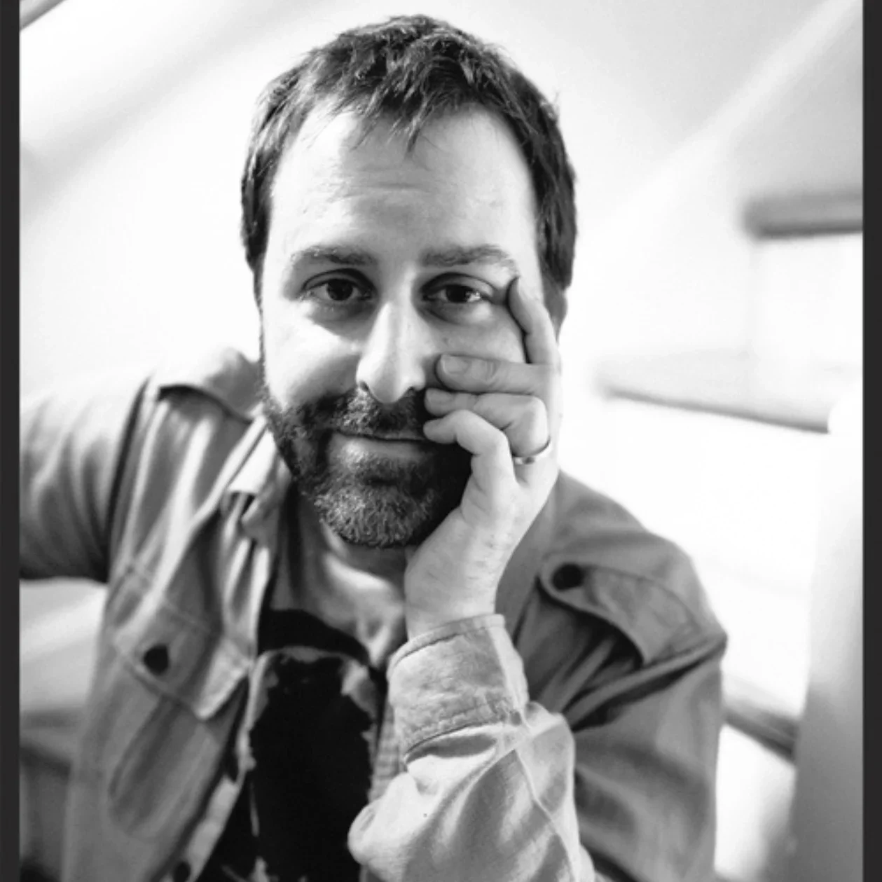 Black-and-white portrait of a bearded man resting his face on his hand.
