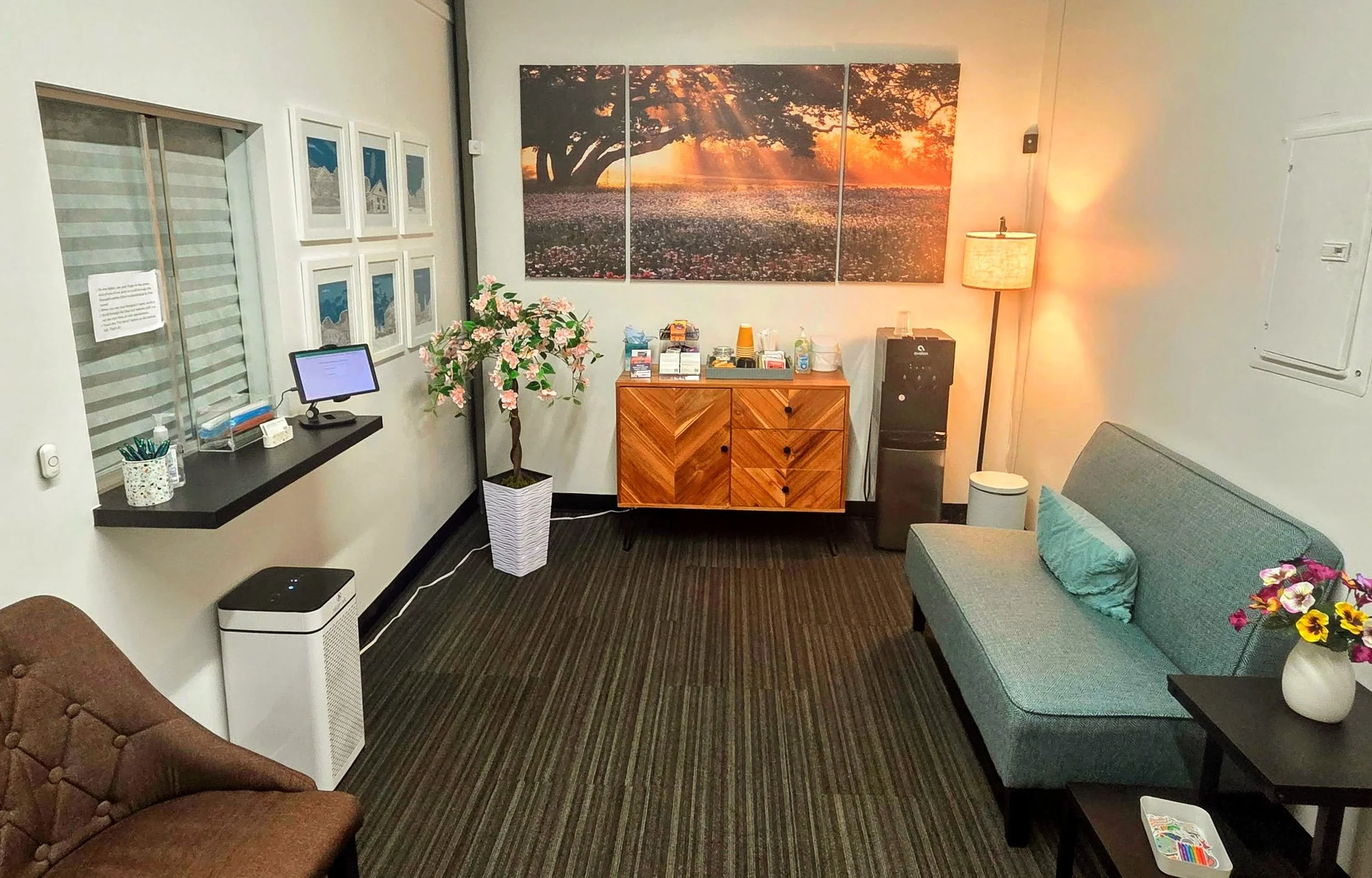 Warm, welcoming counseling office waiting area with a check-in window, seating, soft lighting, and framed wall art.