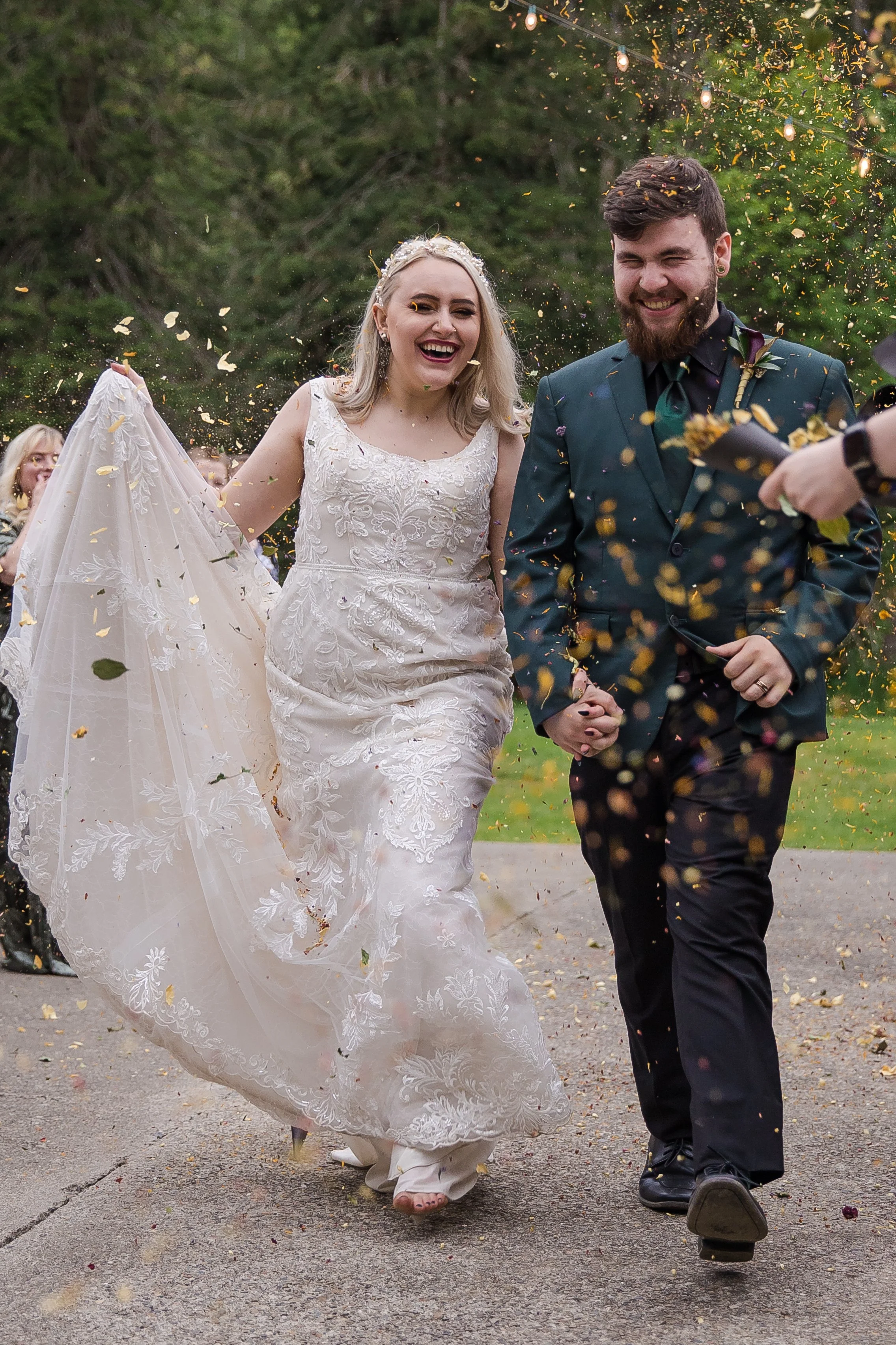 A bride and groom happily walking outdoors during their wedding celebration, surrounded by guests with confetti and lights.
