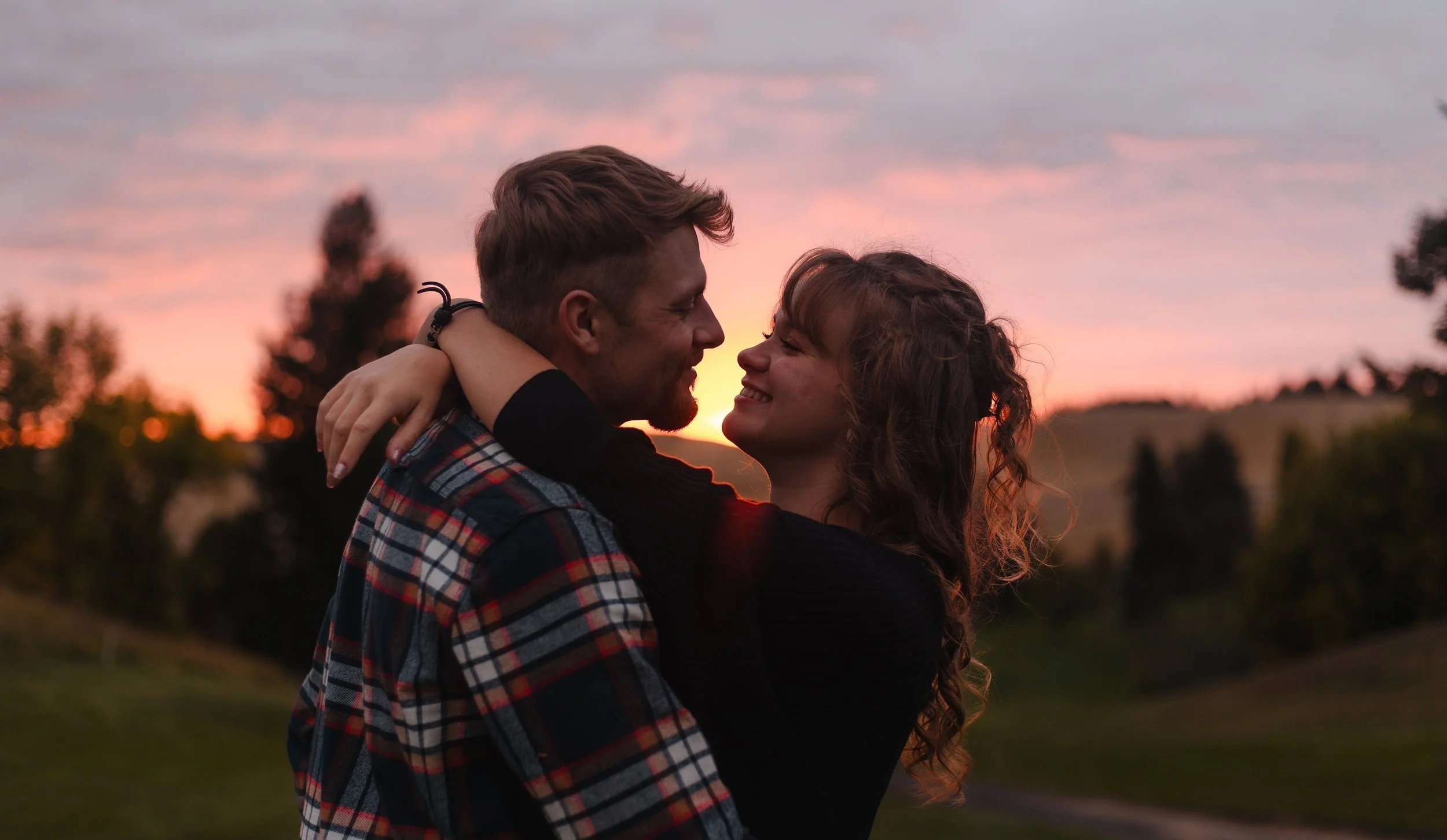 Couple smiling and embracing during outdoor sunset portrait session by LaFleur Photography in North Idaho.