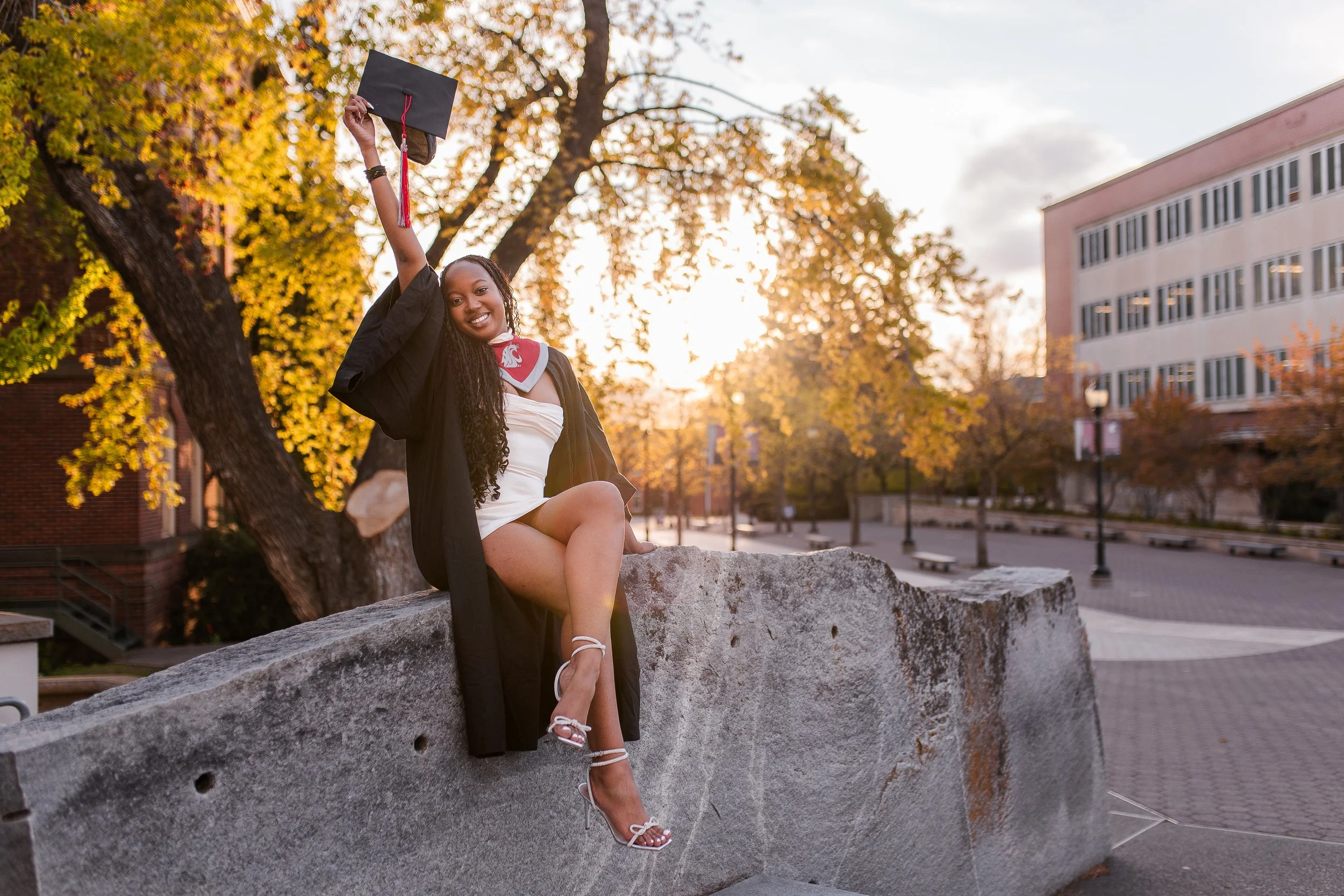 Senior graduation photo of young woman holding cap up in the air to celebrate, during golden hour light, by LaFleur Photography.