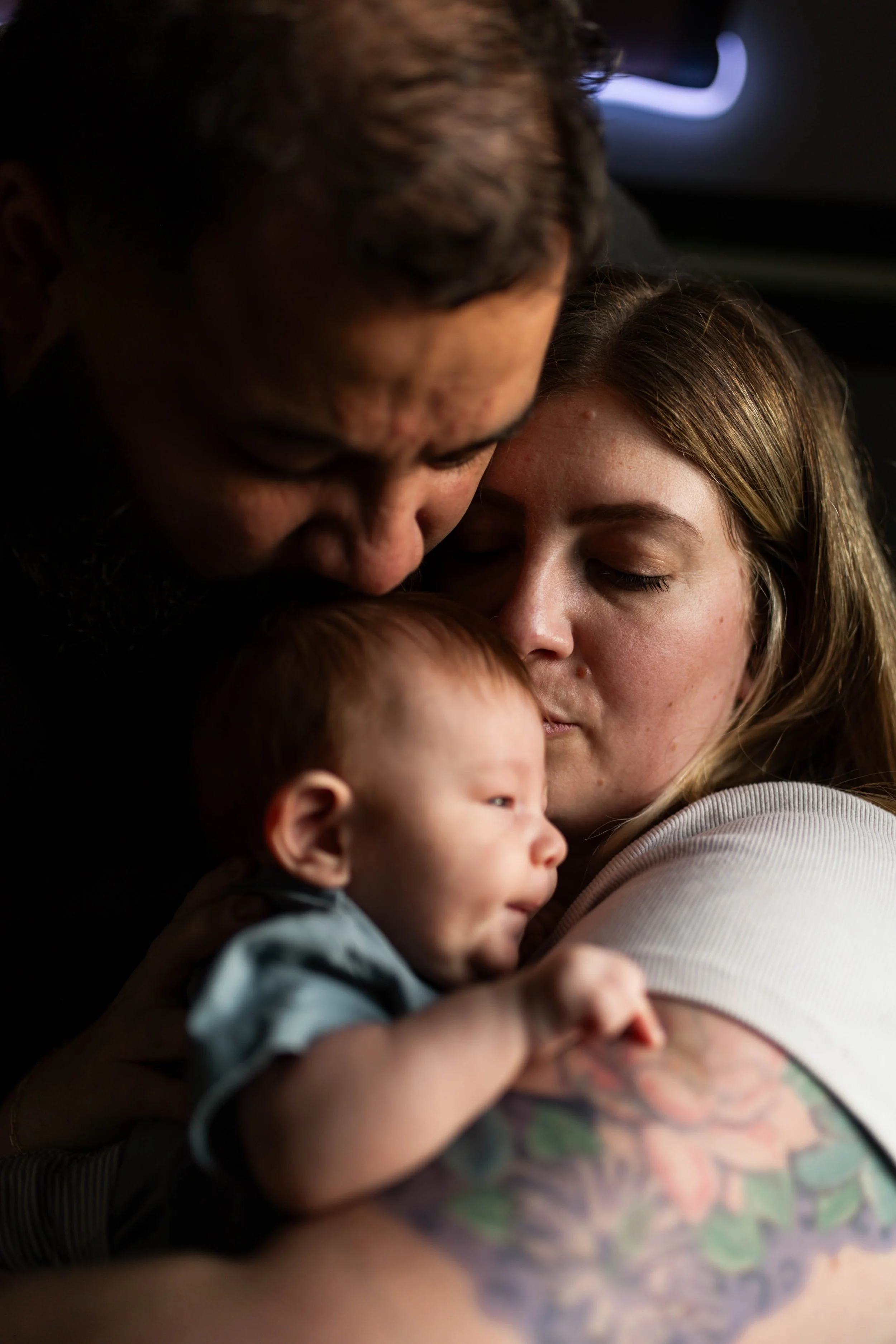 A family moment of a man, woman, and baby sharing an intimate hug and kiss.