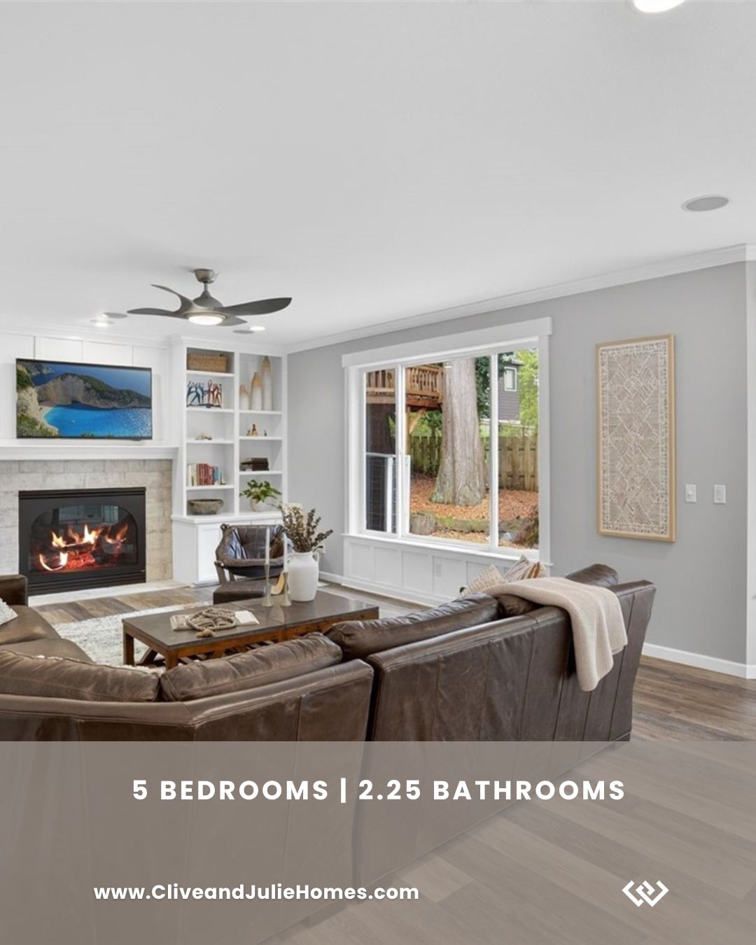 Living room with a large leather sofa, fireplace, TV, white bookshelves, large window showing backyard, ceiling fan, and modern decor.