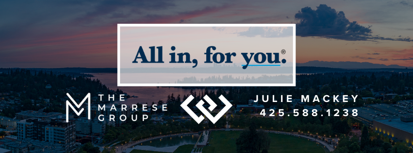 A sunset over a cityscape with a promotional banner for Julie Mackey, a real estate agent, featuring the slogan 'All in, for you' and contact information.