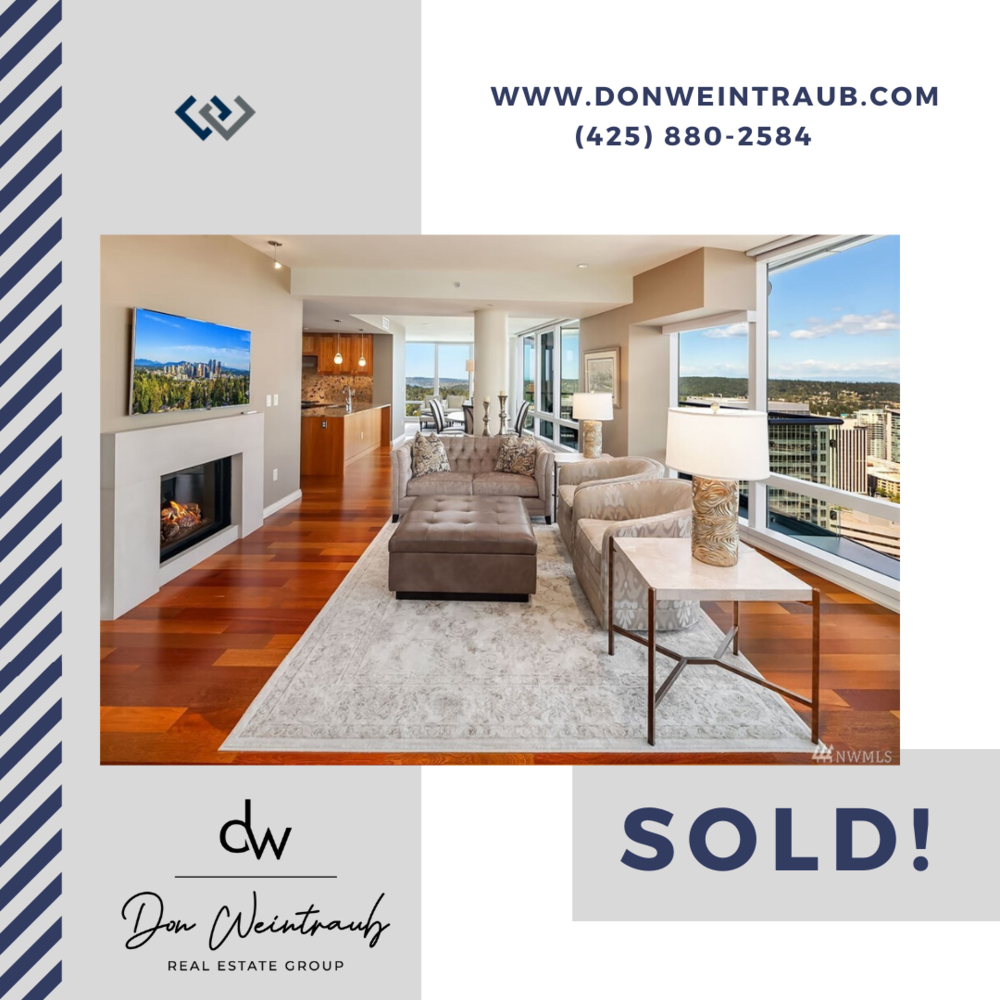 Interior of a modern high-rise apartment with a living room featuring wood floors, a fireplace, a TV, and large windows with city views. The room is decorated with a beige couch, lamps, and artwork.