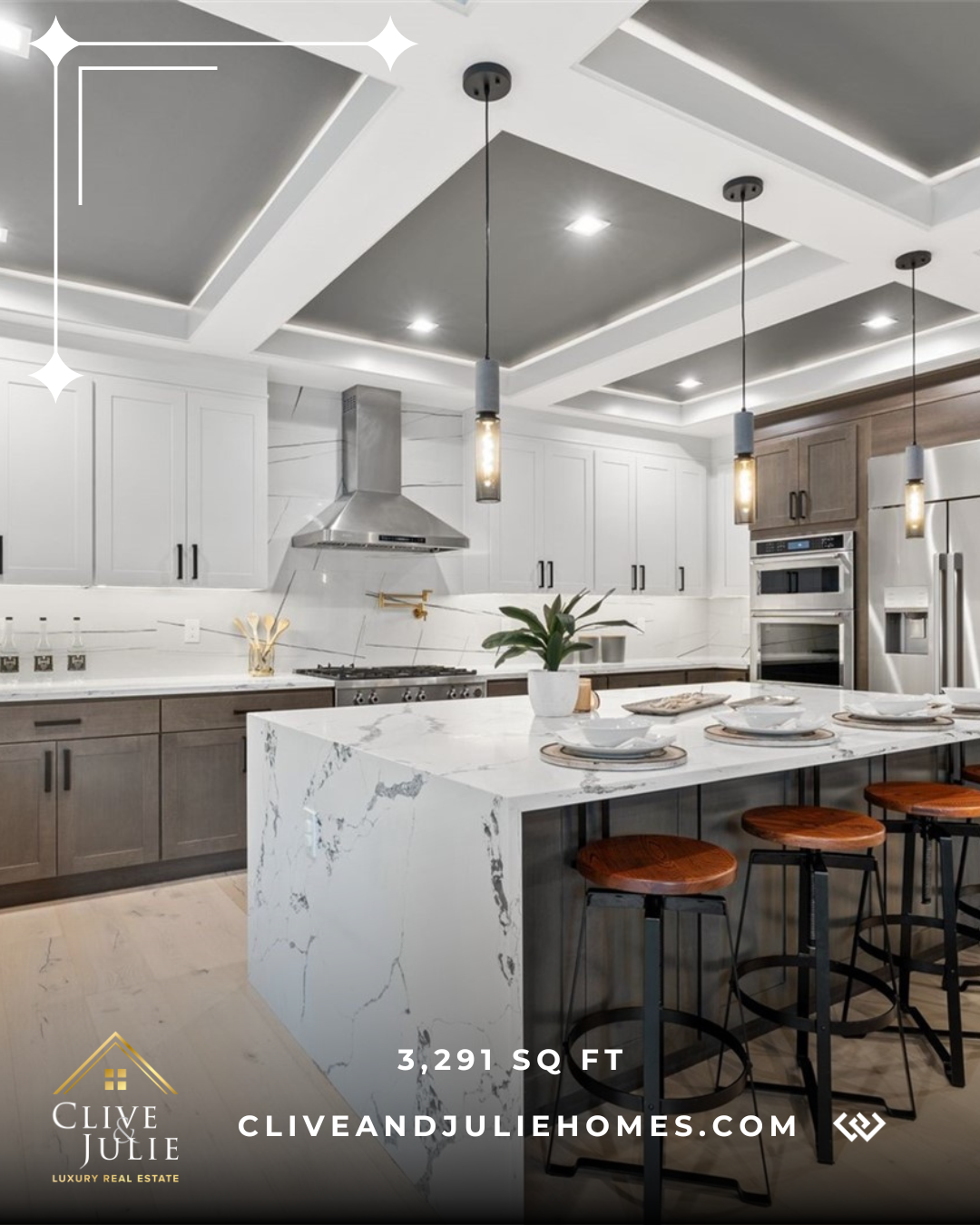 Modern kitchen with white and gray cabinetry, marble island, pendant lighting, stainless steel appliances, and a potted plant on the island.