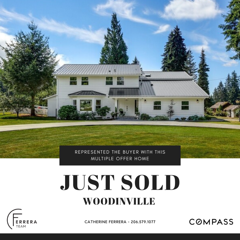 A large white house with a metal roof and front porch, surrounded by green trees and a well-maintained lawn, under a partly cloudy sky.