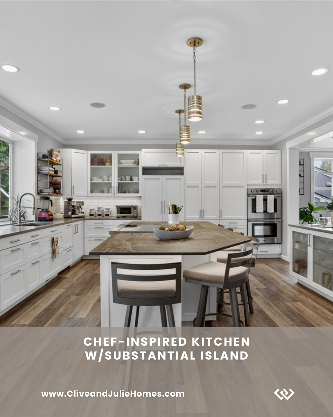 Modern chef-inspired kitchen with white cabinets, a large central island with a substantial countertop, pendant lighting, and stainless steel appliances. Contains small kitchen appliances and decorative items.