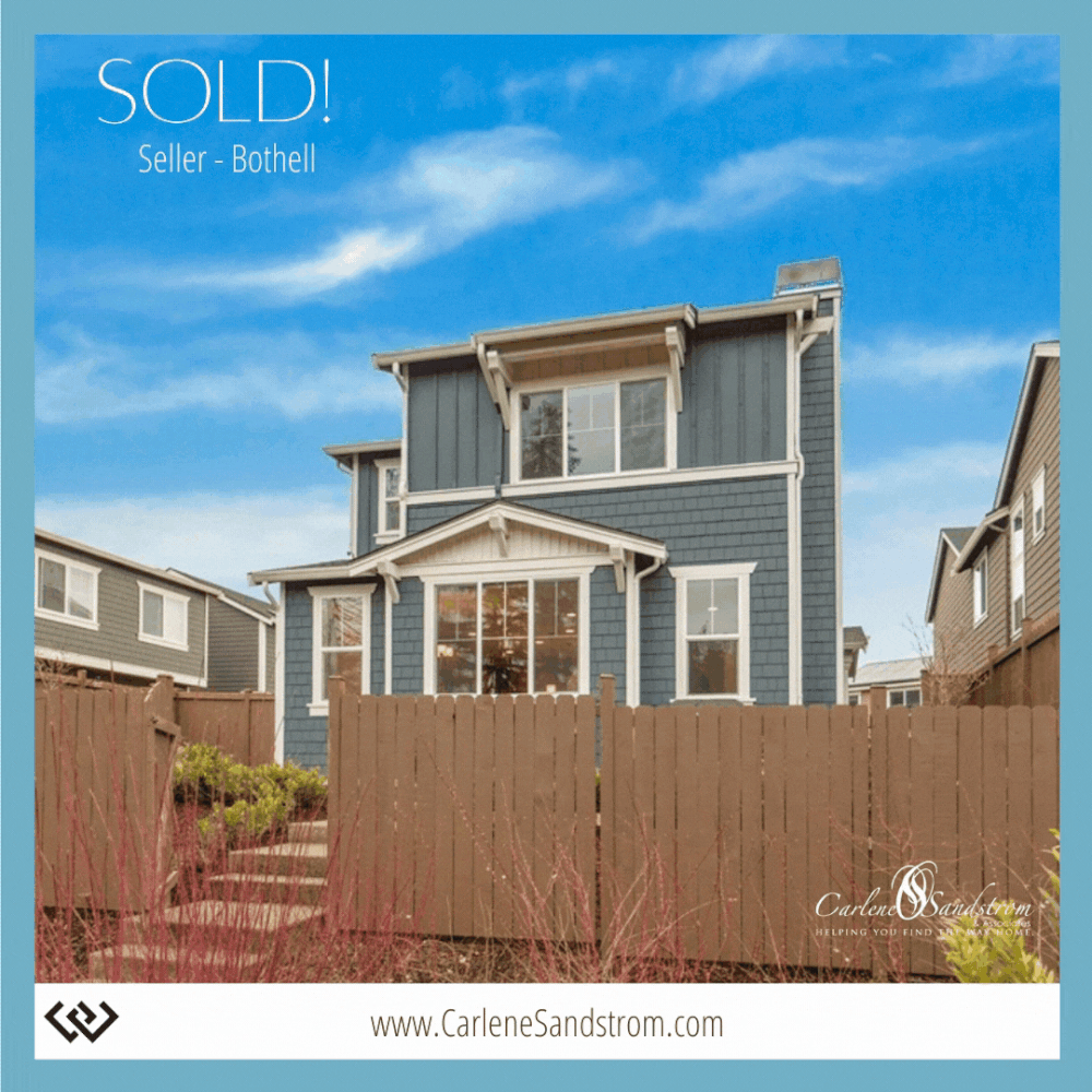 A blue multi-story house with white trim behind a brown wooden fence, with a clear blue sky in the background and a 'SOLD!' sign on the property.