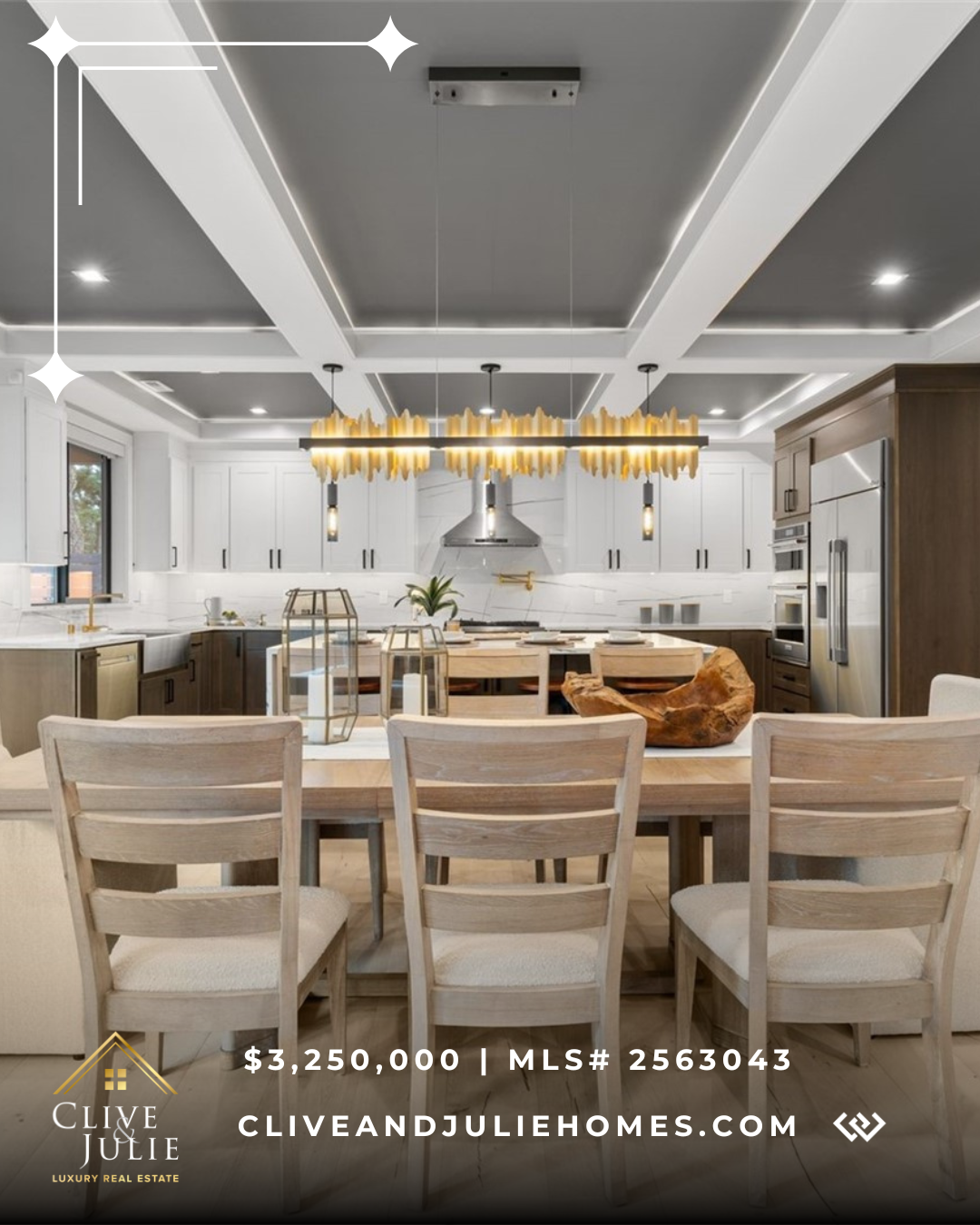 Modern kitchen with white cabinets, stainless steel appliances, and a large wooden dining table with six chairs. Overhead lighting fixture with yellow accents hangs above the table.