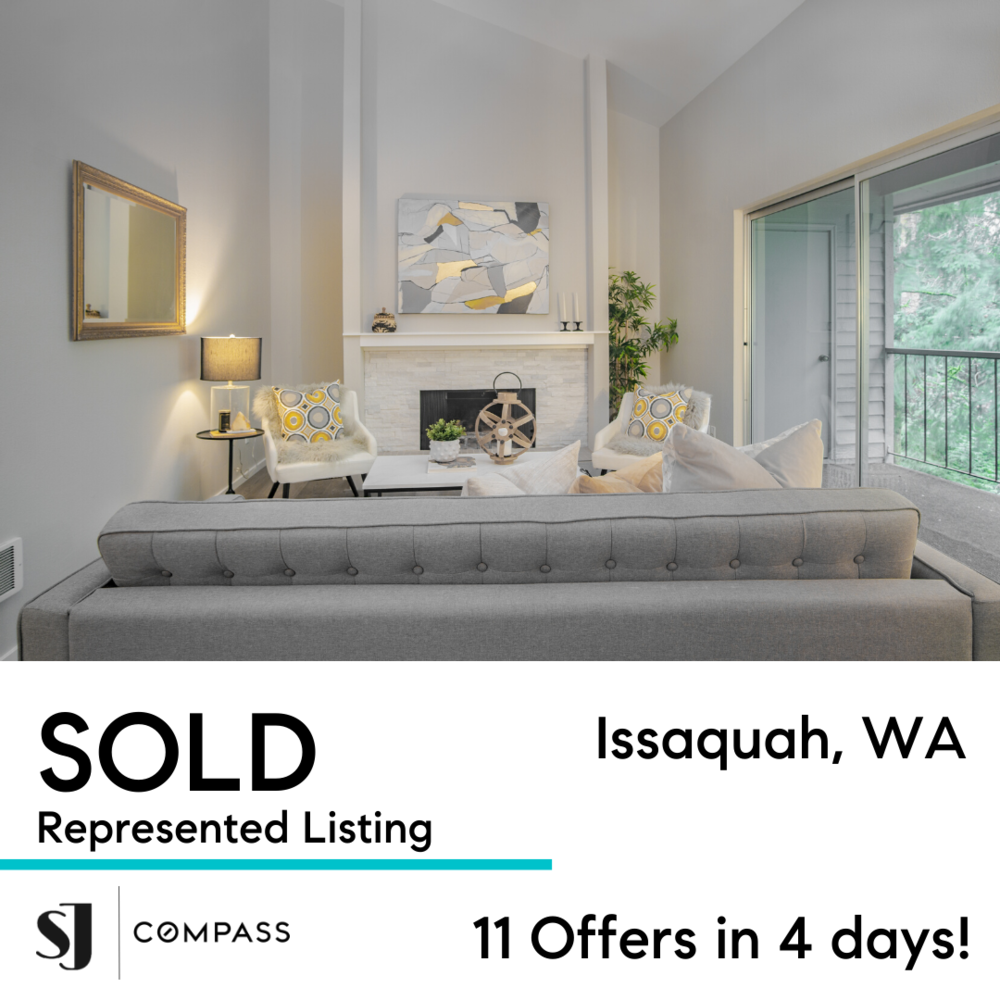 Living room with white walls, a fireplace, a gray upholstered sofa, two white armchairs with yellow and gray patterned pillows, a side table with a lamp, decorative items on the mantel, and a balcony with a sliding glass door showing outdoor greenery