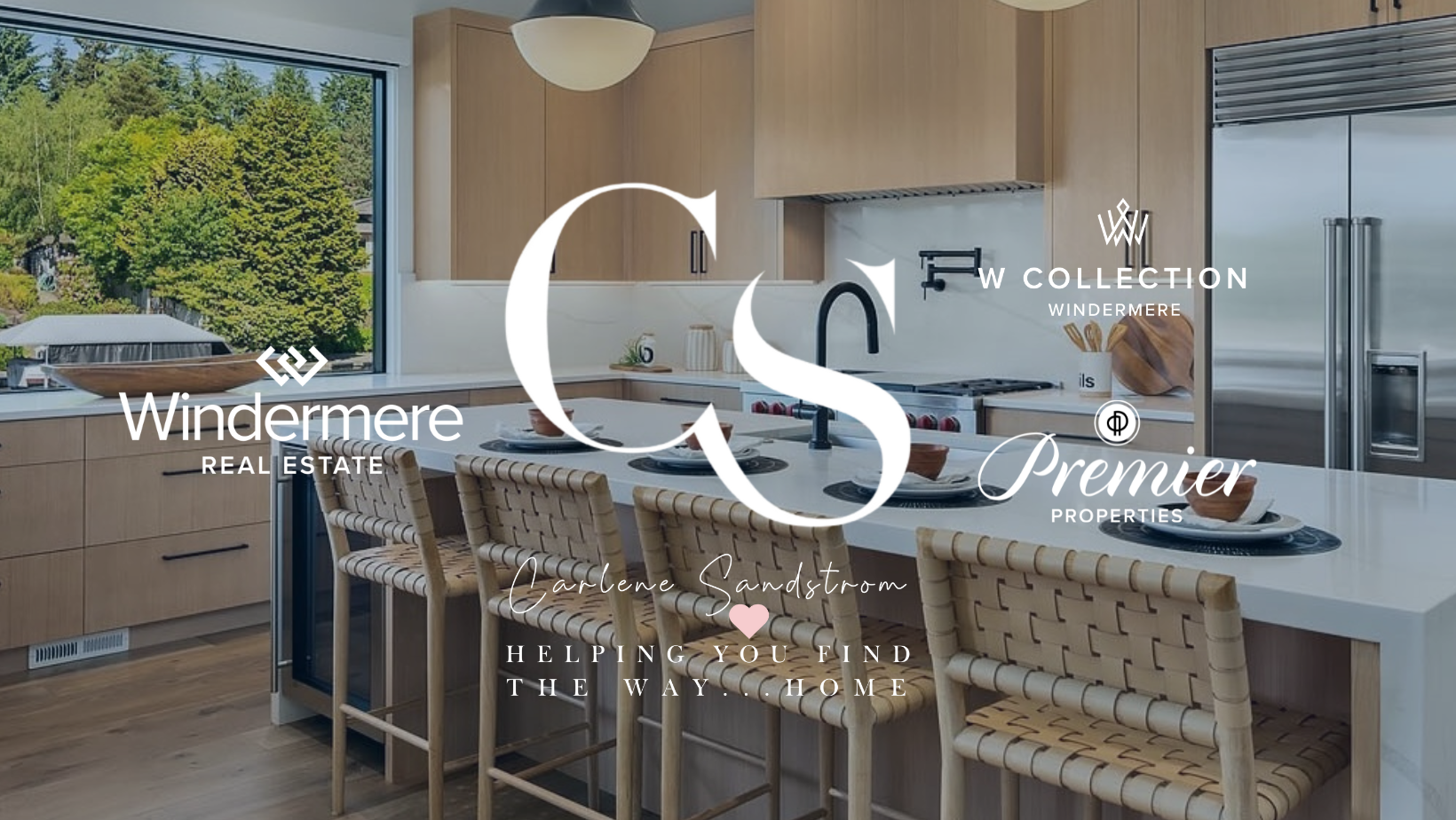 Modern kitchen with wooden cabinets, white countertop, large window showing greenery outside, and beige woven chairs around a kitchen island.