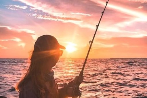 Person fishing at sunset on the ocean with a fishing rod.
