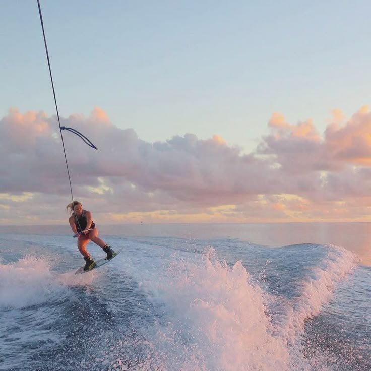 A person wakeboarding on the ocean during sunset, holding onto a tow rope.