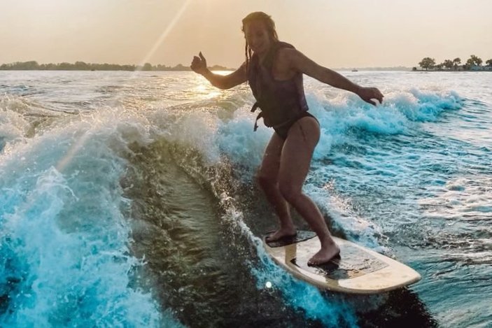 Woman surfing on a wave during sunset, wearing a life jacket.