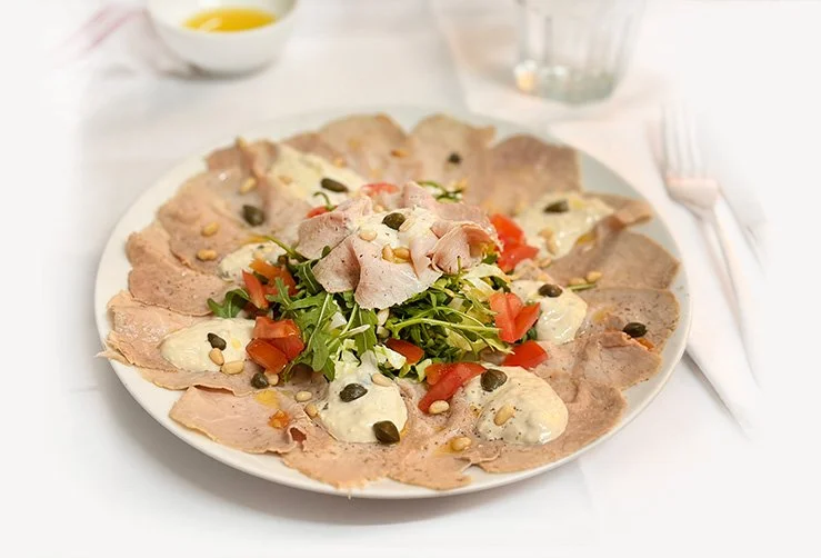 Een ronde salade met plakjes vlees, tomaten, sla en een dressing