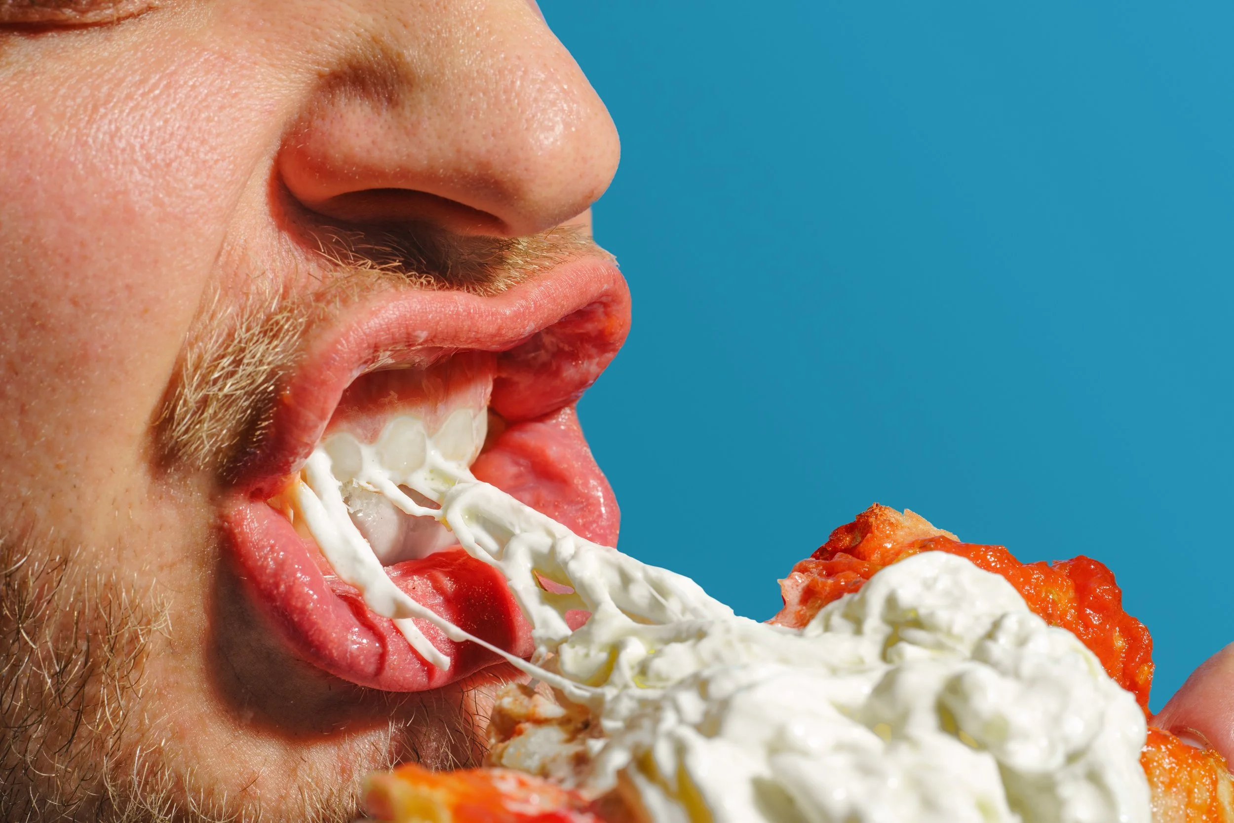 Uomo che mangia una pizza con panna, formaggio e pomodoro, con sfondo blu.
