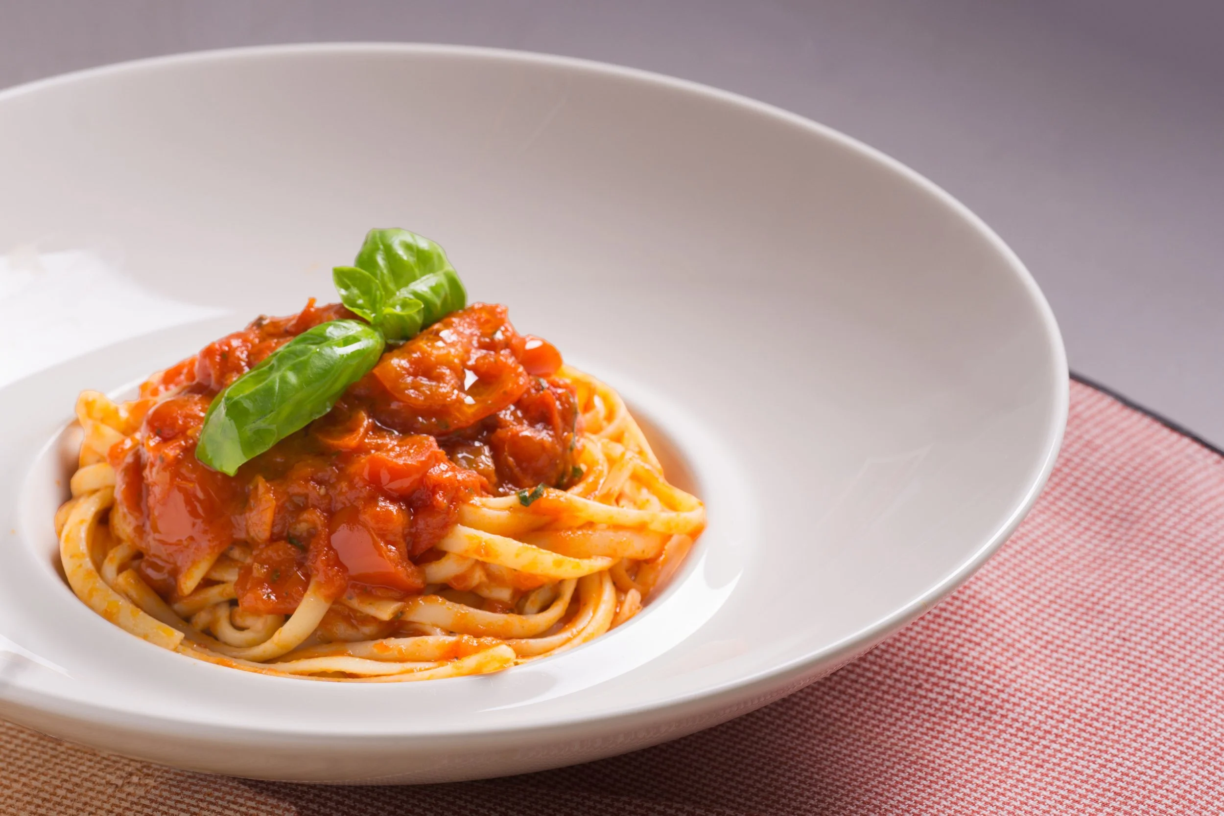 Piatto di spaghetti con salsa di pomodoro e basilico in una ciotola bianca.