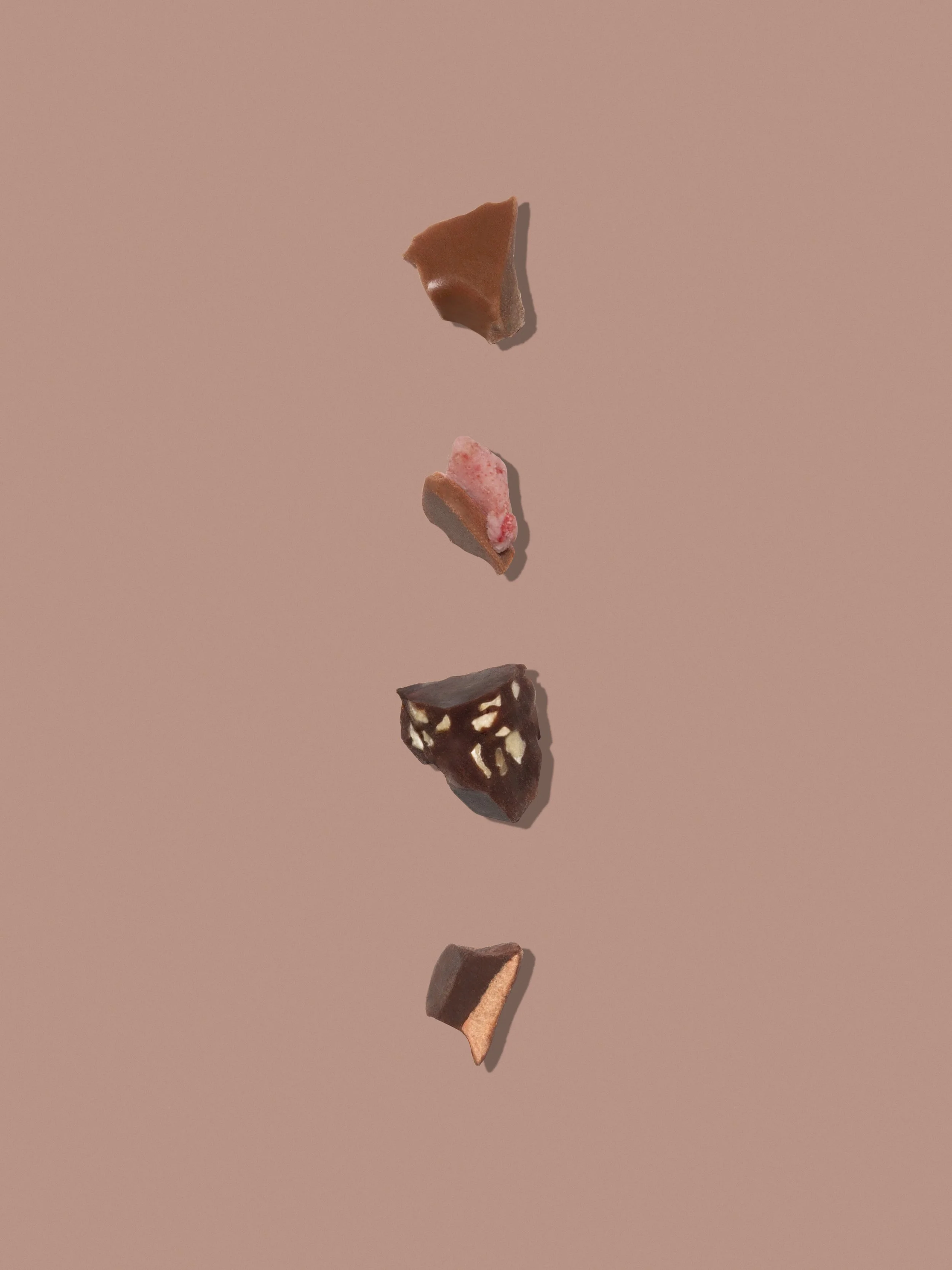 Petite composizione di pezzi di cioccolato di diversi gusti e colori disposti in una fila verticale su sfondo rosa