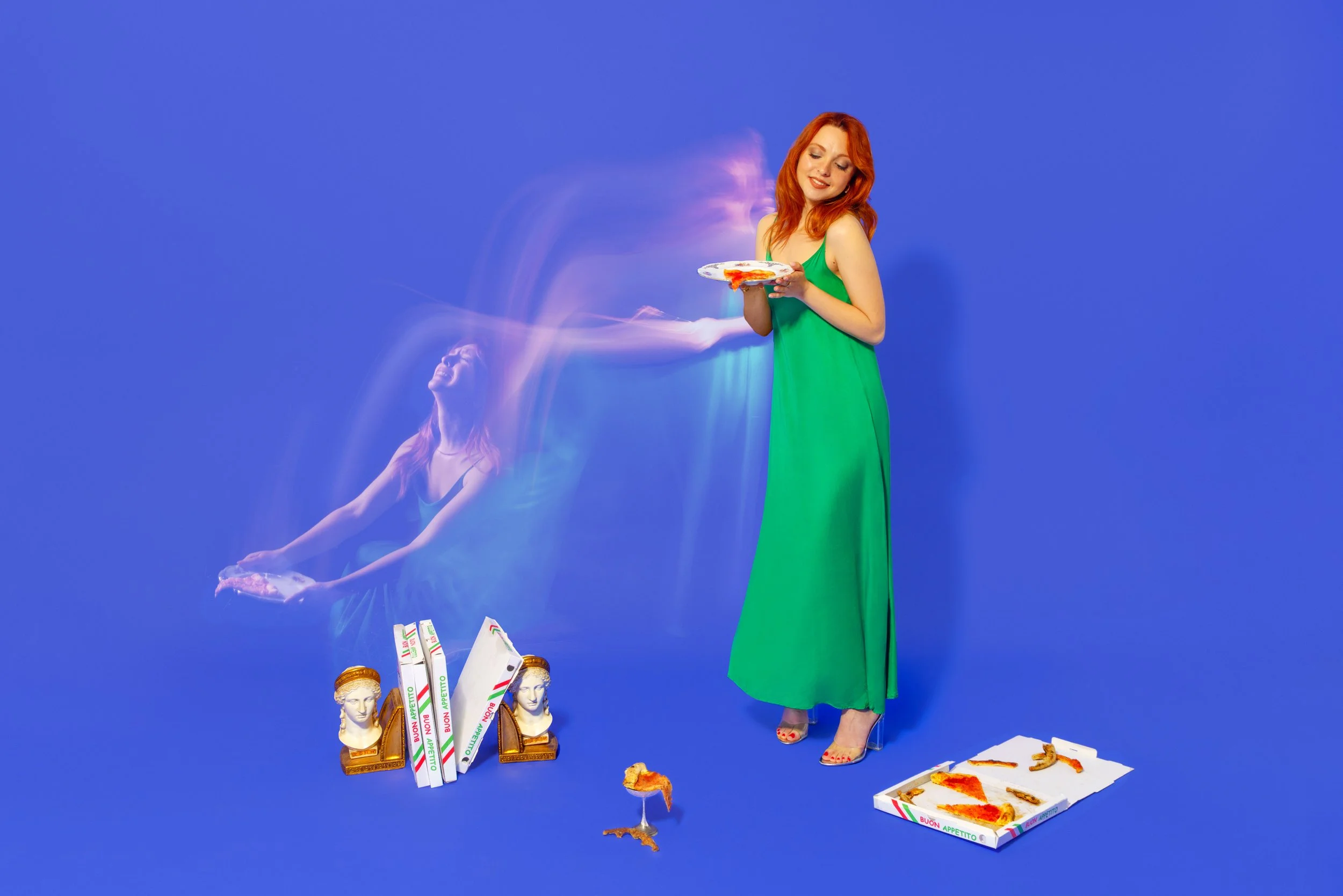 Donna con capelli rossi in abito verde che tiene una fetta di pizza, con elementi decorativi come statue antiche e scatole di pizza con scritte in italiano, su uno sfondo blu.