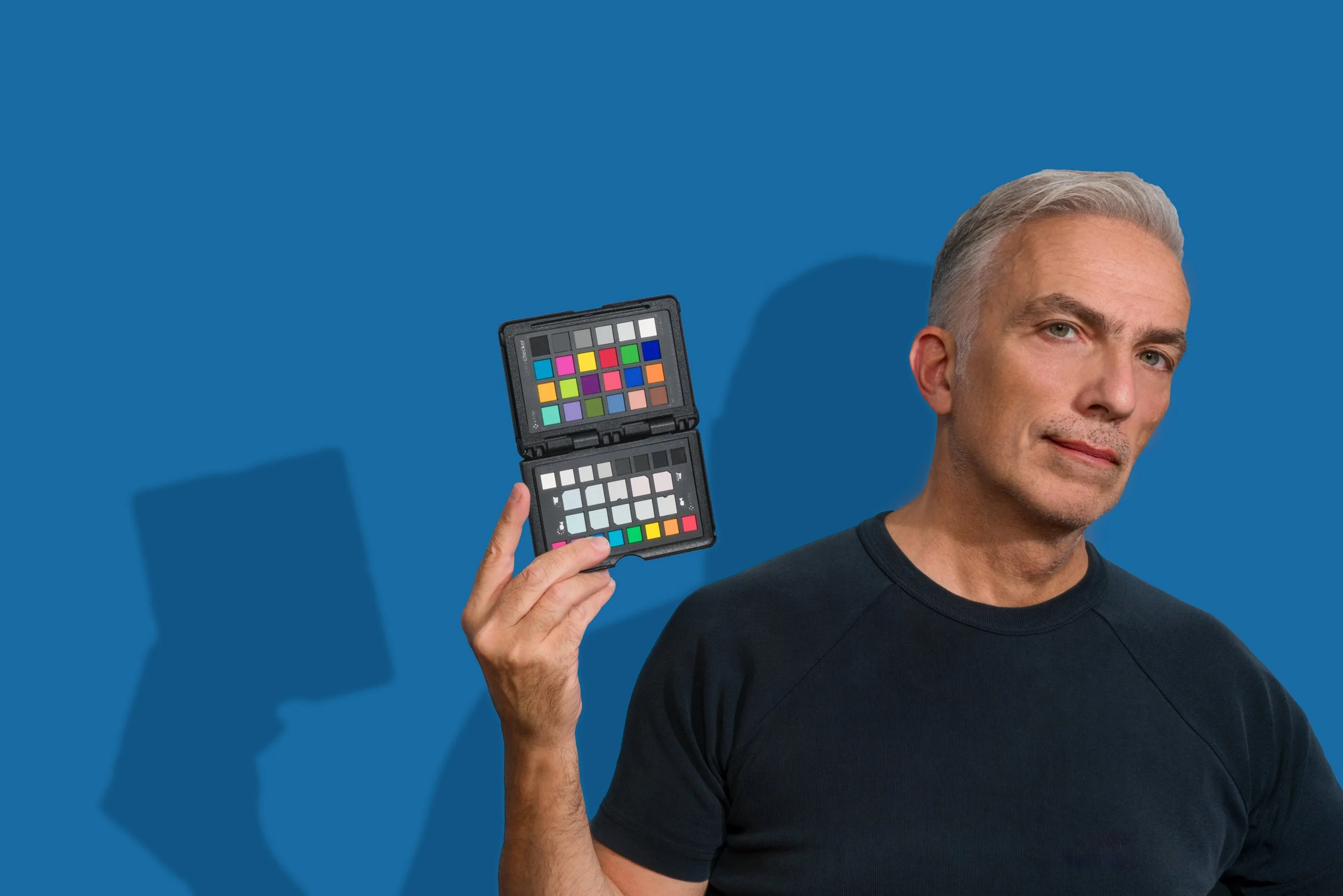 Uomo con capelli grigi chiaro che tiene un color chart con vari campioni di colori di fronte a uno sfondo blu.