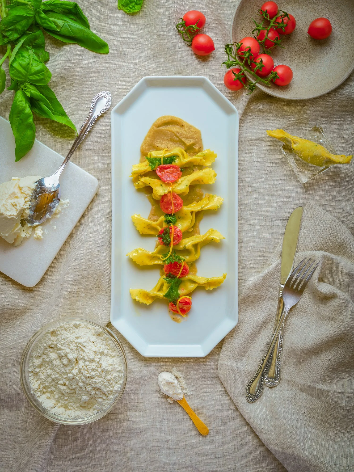 Piatti di pasta con pomodorini, crema di piselli, basilico, e ingredienti da cucina come farina e formaggi sulla tovaglia, che prepara una ricetta italiana.