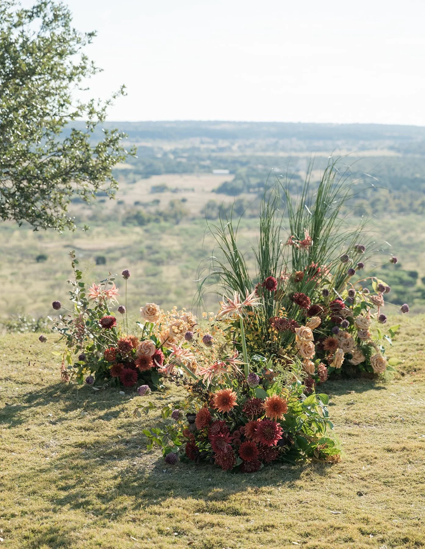 Ranch wedding ceremony overlooking stunning views and ceremony florals staggered with greens, burgundy’s, blushes, mauves for a wild and organic look by Remi & gold austin texas florists 