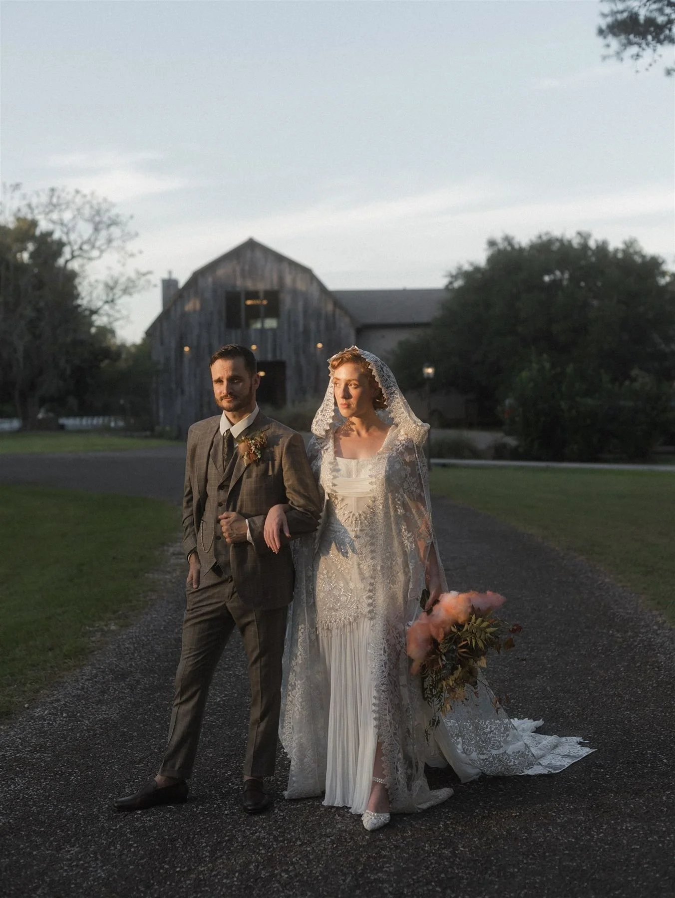 Moody sunset photos of bride and groom arms linked at the historic hill house wedding venue north of houston - groom in suit with peaky blinders aesthetic, wool suit and bride in couture bridal dress with lace cape