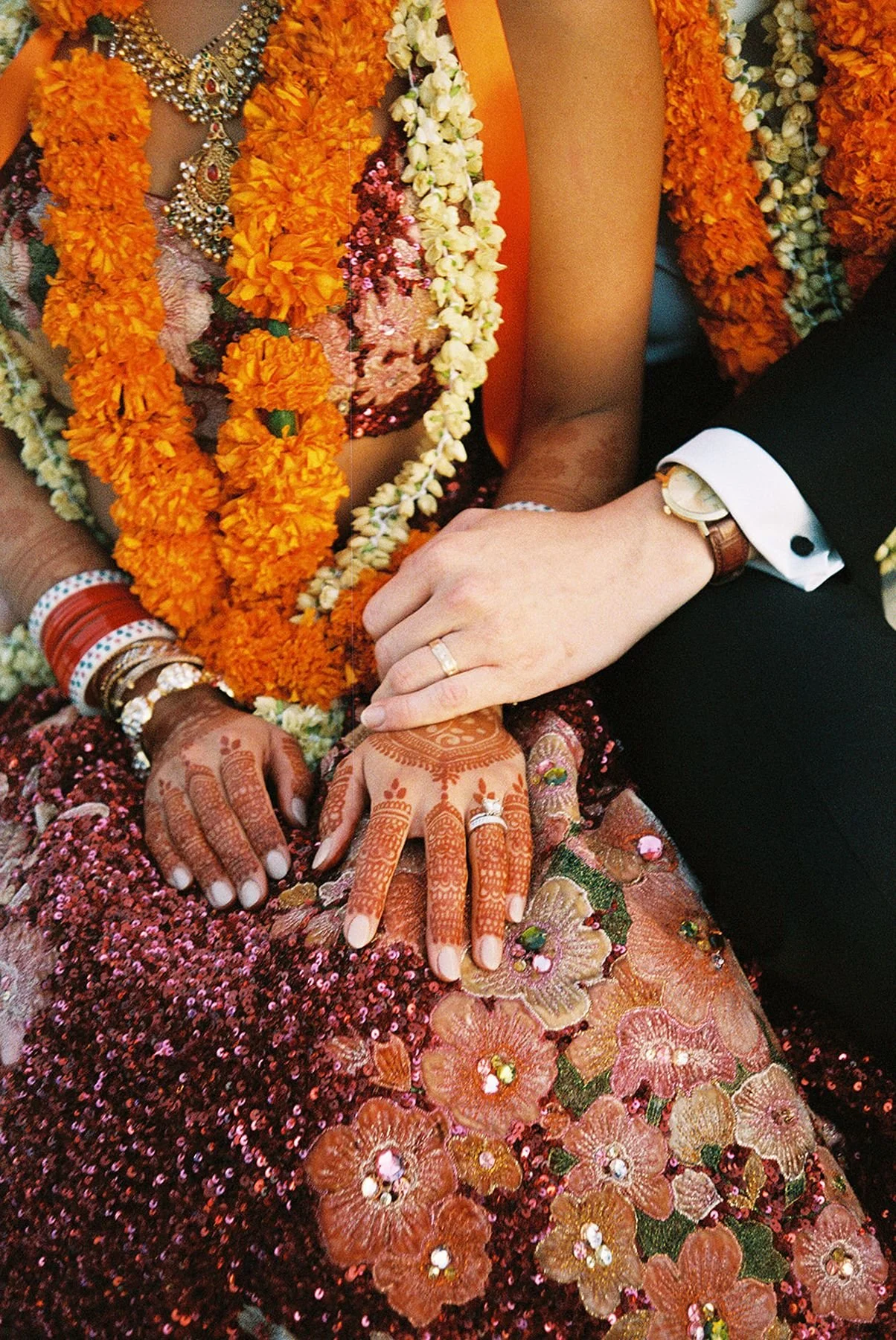 Closeup details of a Hindu Indian bride with heirloom jewelery, henna, marigold strands, couture sabyasachi red gown